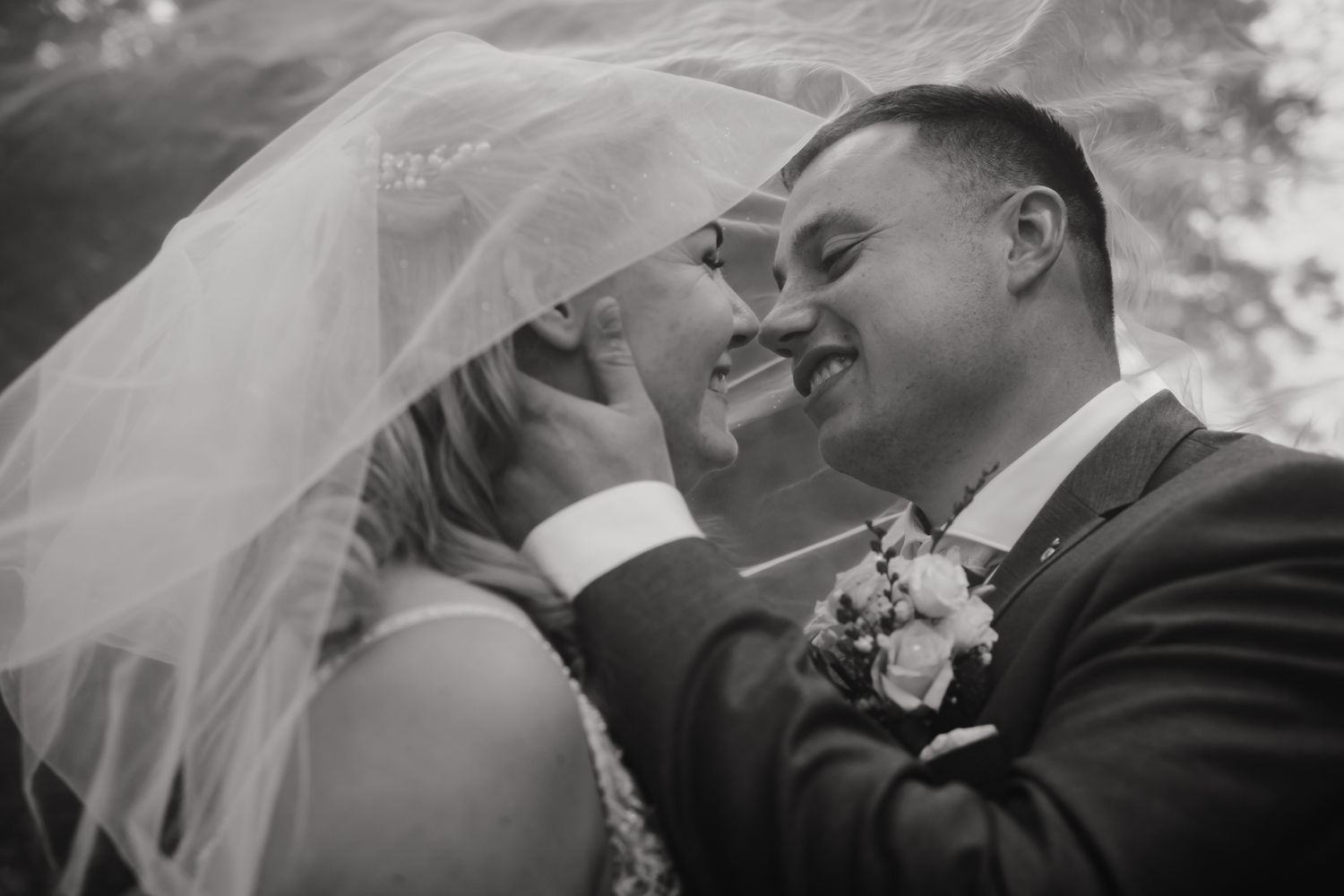 Black and white close-up of romantic wedding moment with flowing veil.