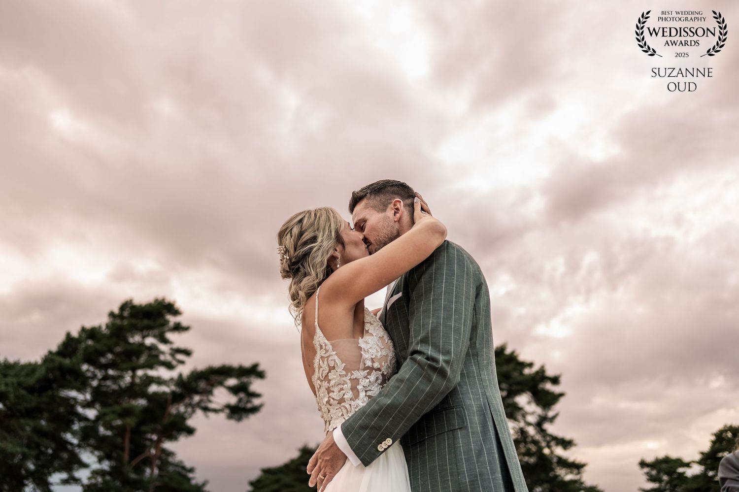 A couple shares a romantic embrace during their wedding photoshoot under dramatic cloudy skies.