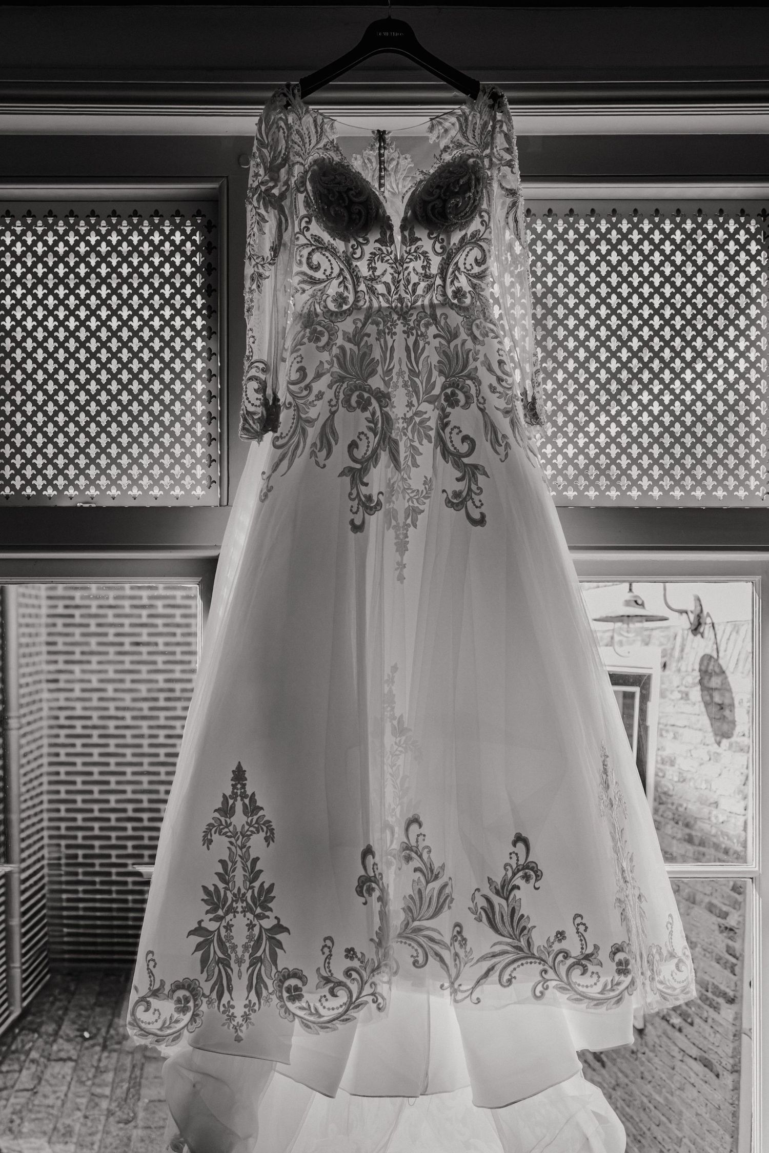 Black and white photograph of an elegant white wedding dress with intricate embroidery displayed on a mannequin.