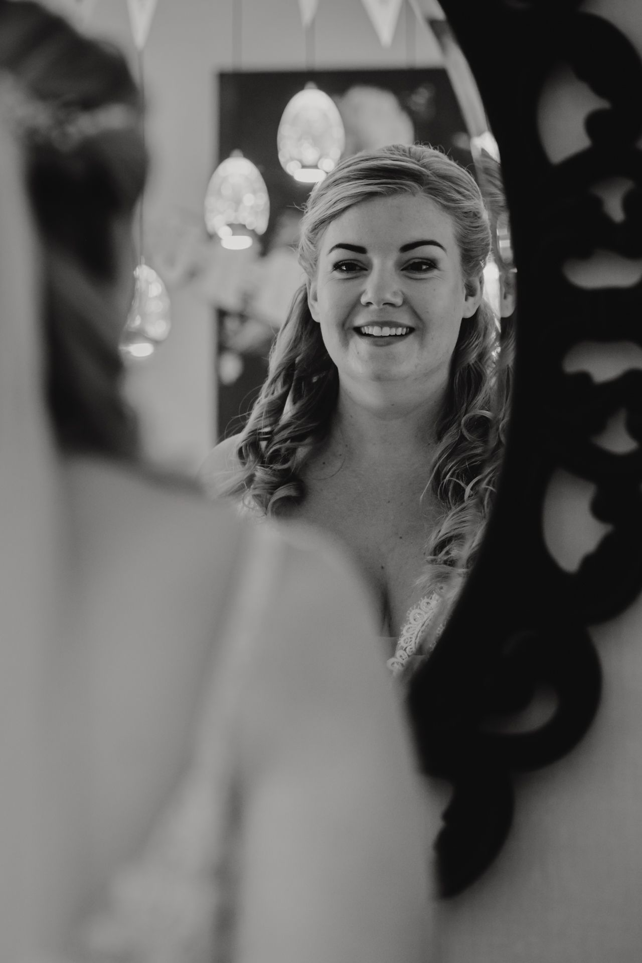 Black and white reflection of a bride smiling in an ornate mirror on her wedding day.