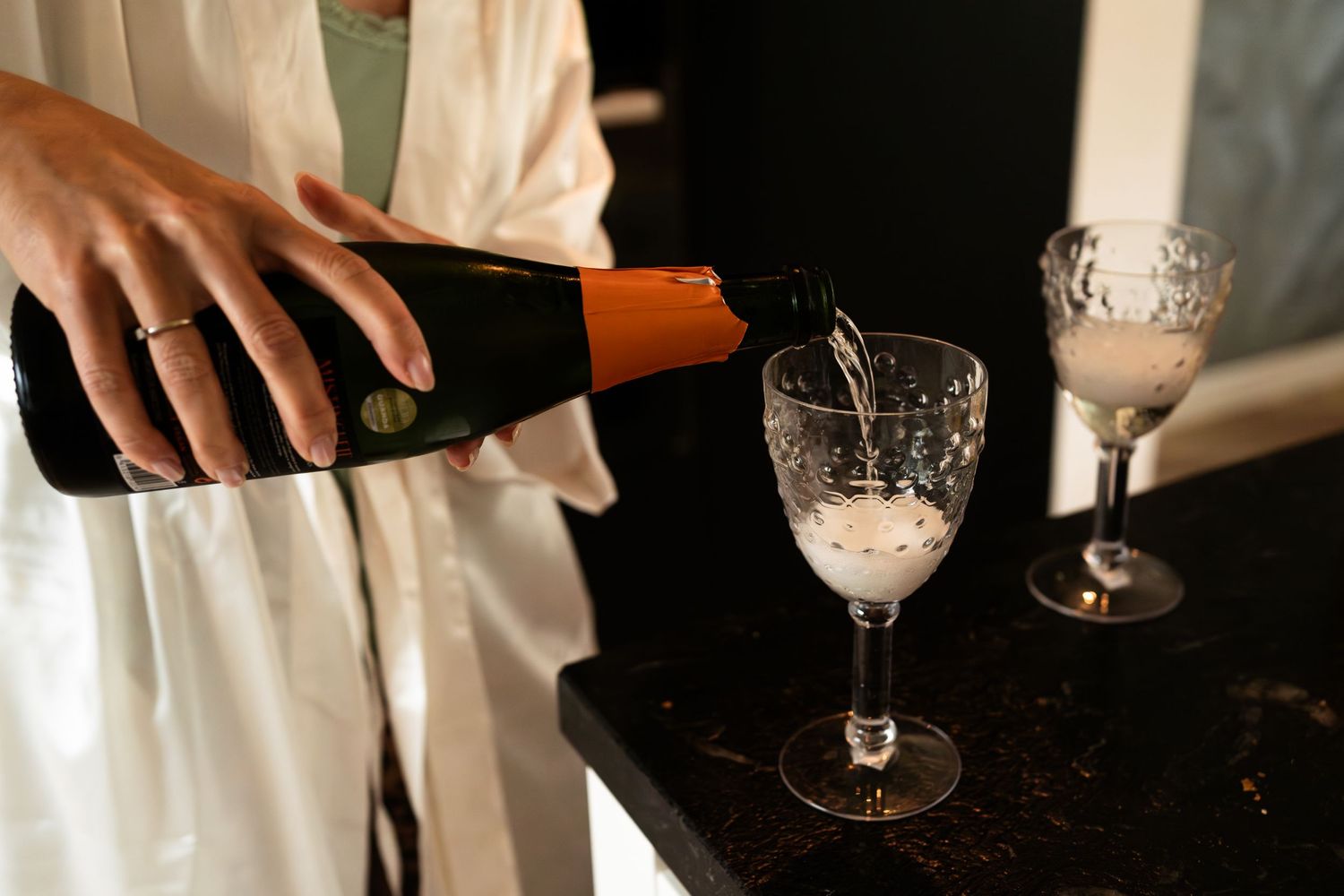 Someone pouring champagne into elegant crystal glasses on a dark table for a celebration.