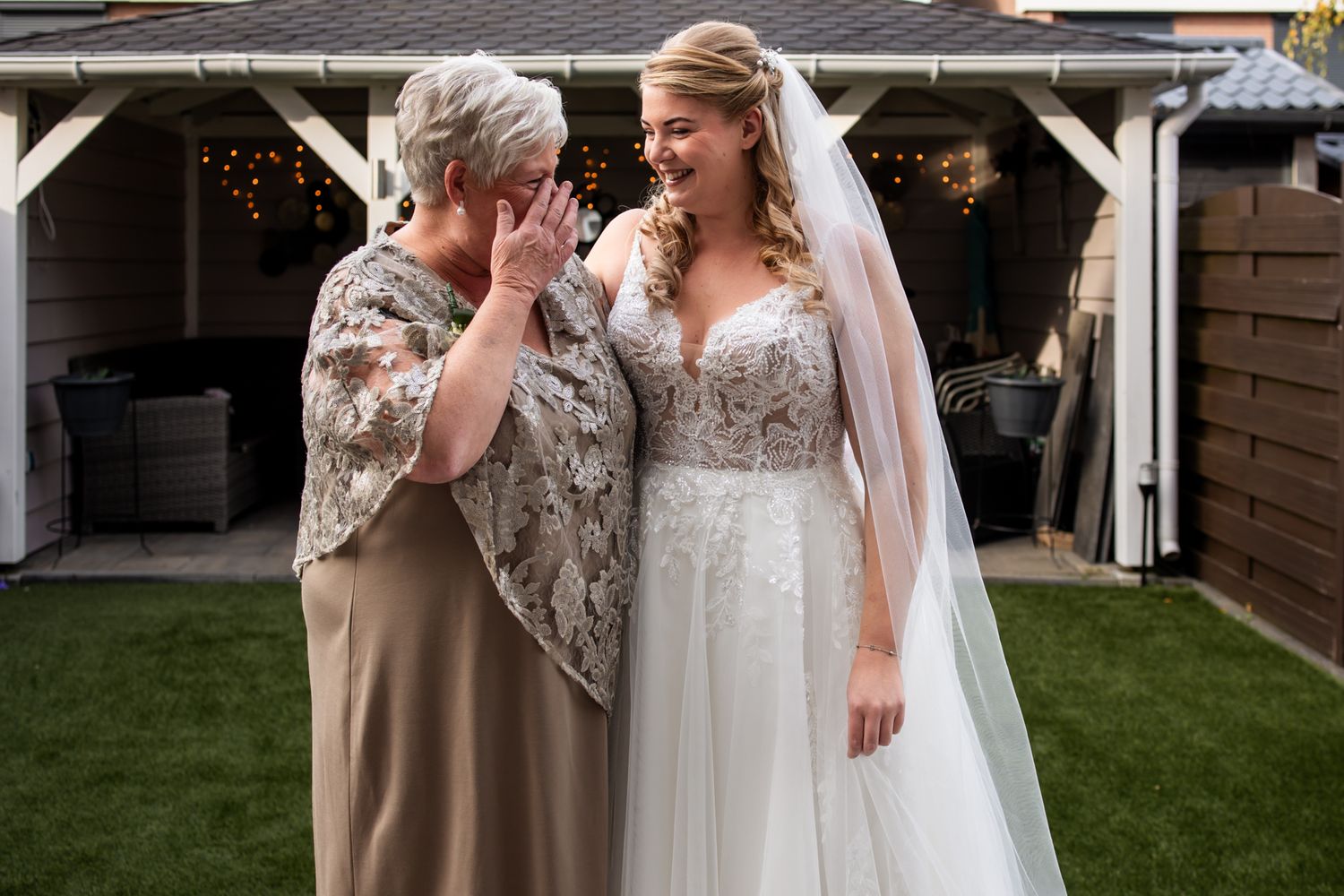 An emotional mother and bride share a touching candid moment in a garden setting during a wedding celebration.