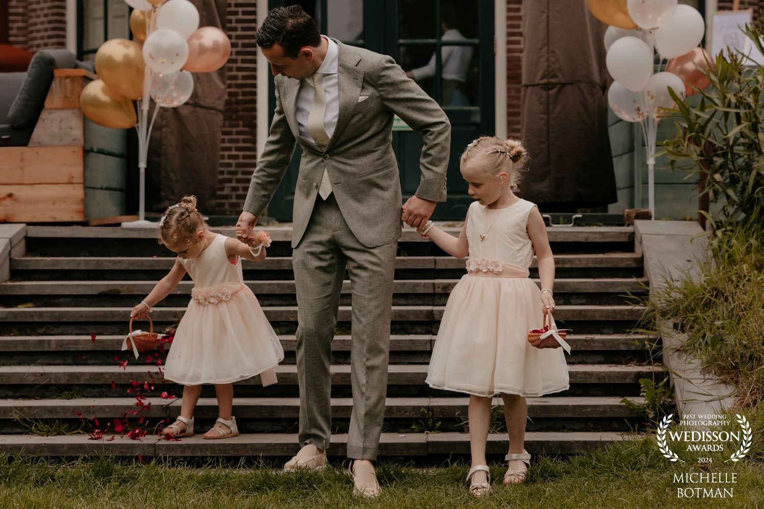 Outdoor wedding scene with balloons on brick steps and dressed-up group on stairs.