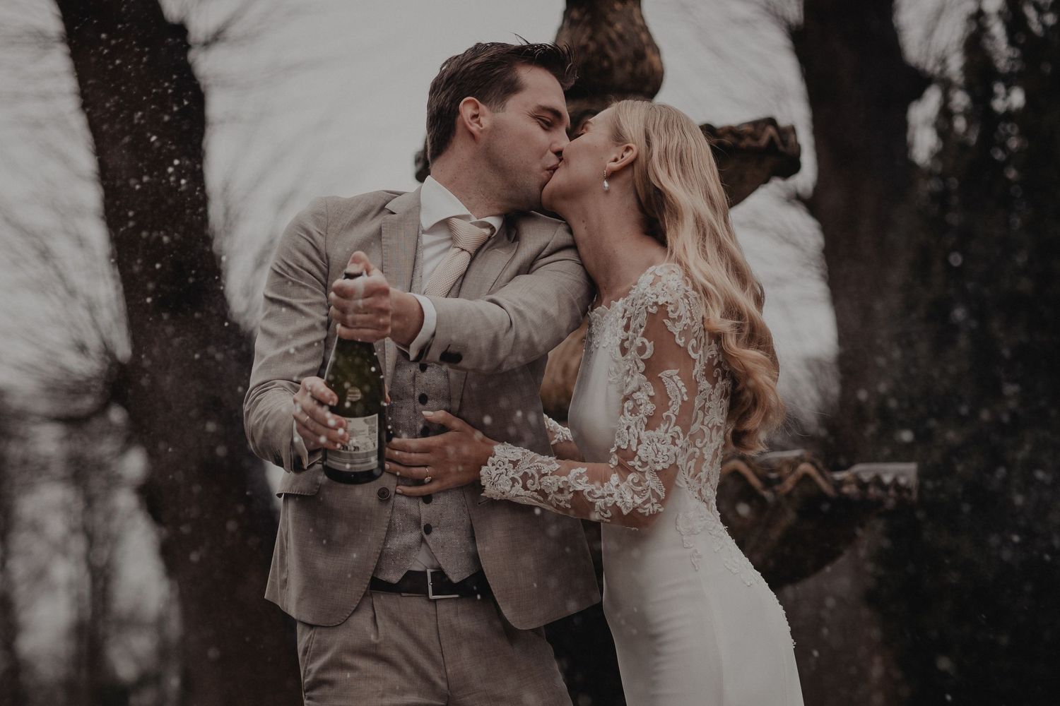 A romantic couple embraces and shares a kiss in a wooded outdoor setting during a wedding ceremony.