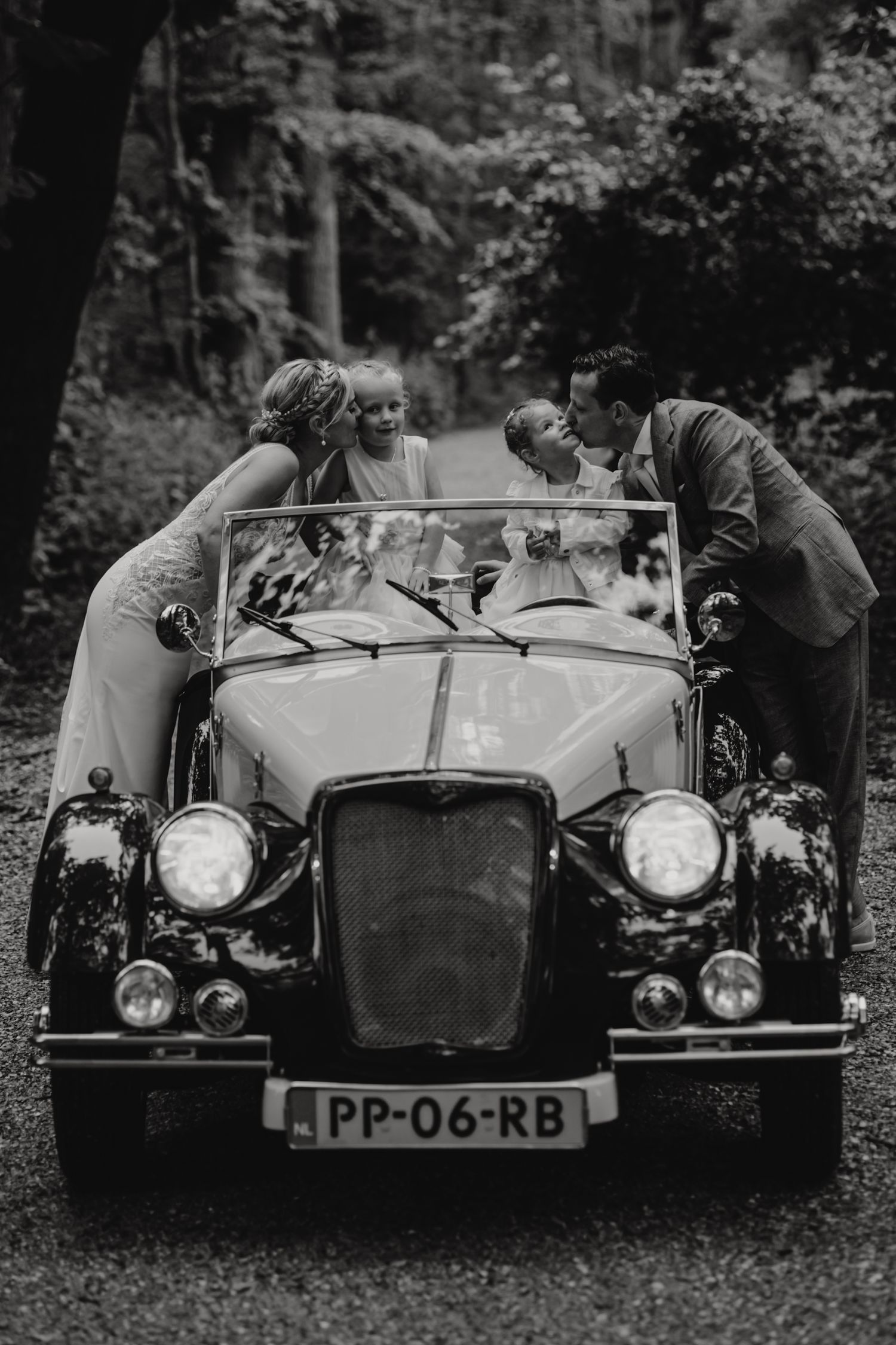A vintage convertible car photographed in a wooded forest setting.