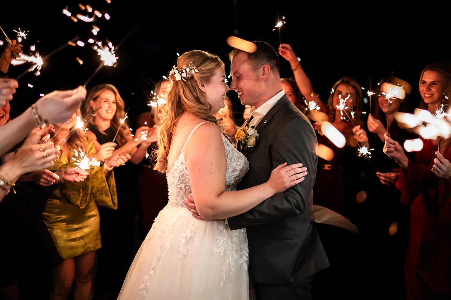 Wedding couple shares romantic kiss during sparkler exit sendoff with guests lighting the night with sparklers.