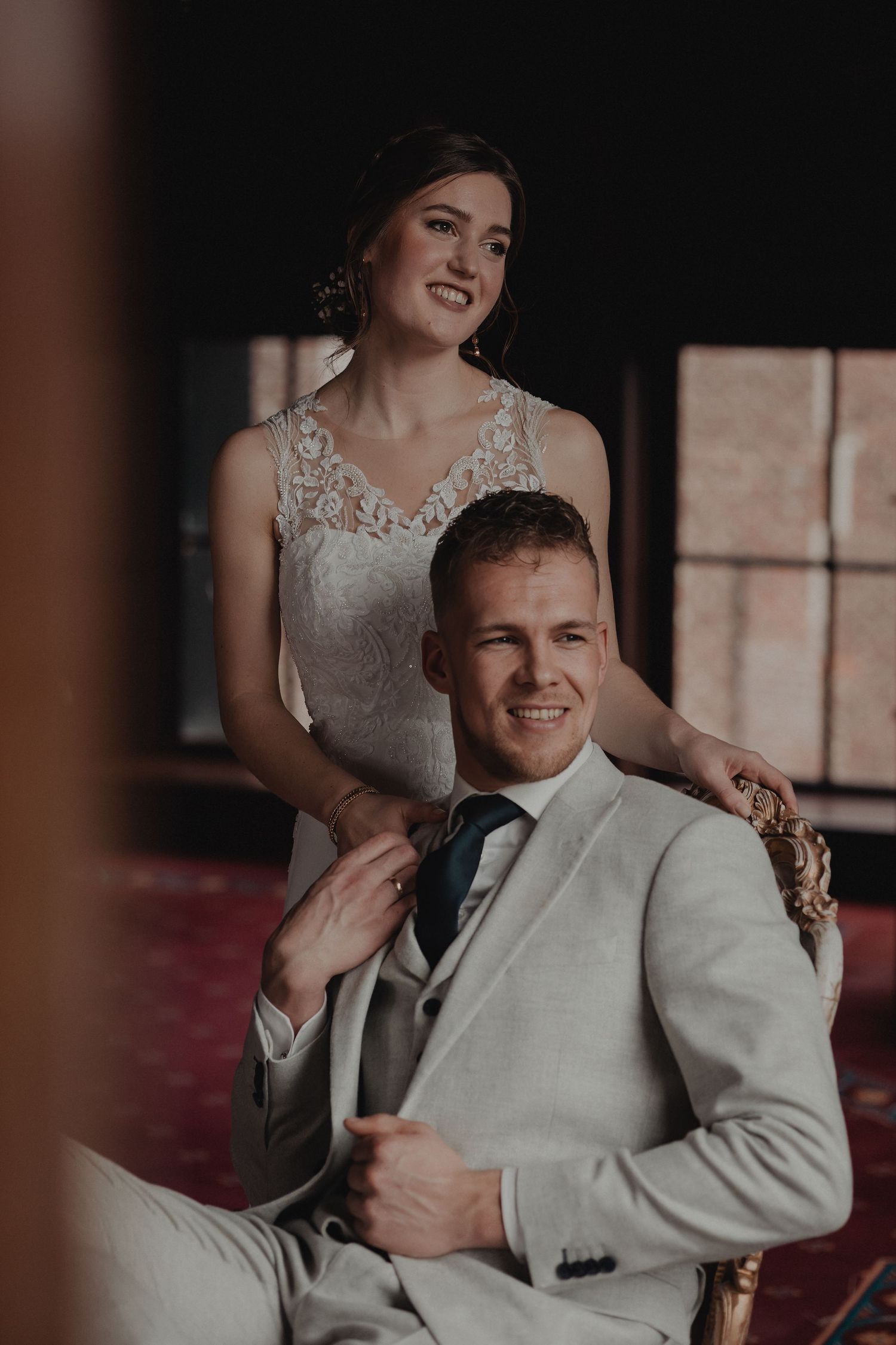 A wedding couple shares a tender moment in formal attire against a rustic indoor backdrop.