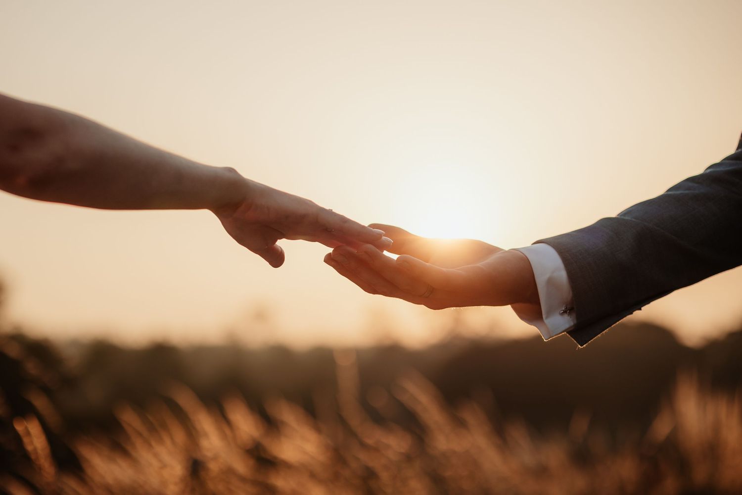 Two hands gently touching fingertips at golden sunset, romantic couple connection moment in warm outdoor light.