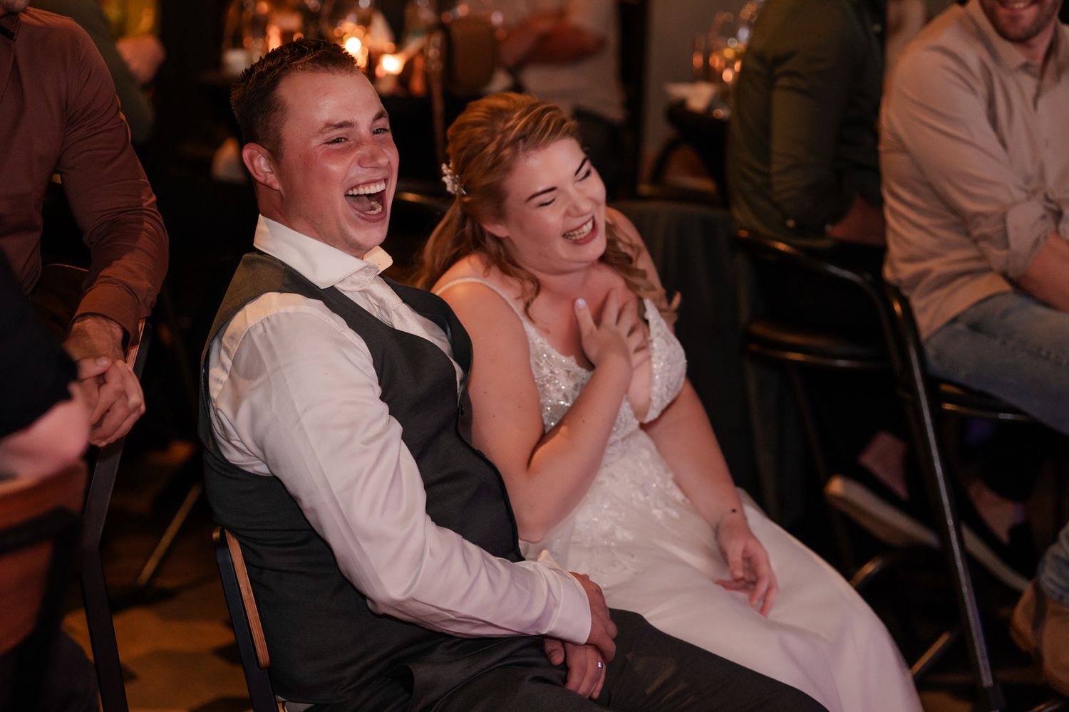 Two people share a laugh together while seated at a wedding reception in formal attire.