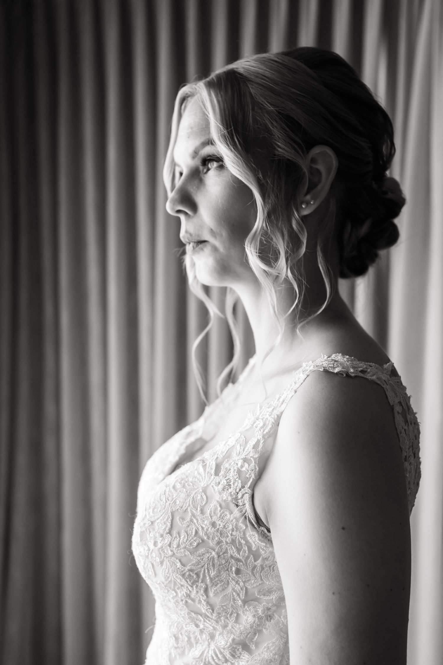 Elegant black and white portrait of a bride in a lace wedding dress looking to the side with an updo hairstyle.