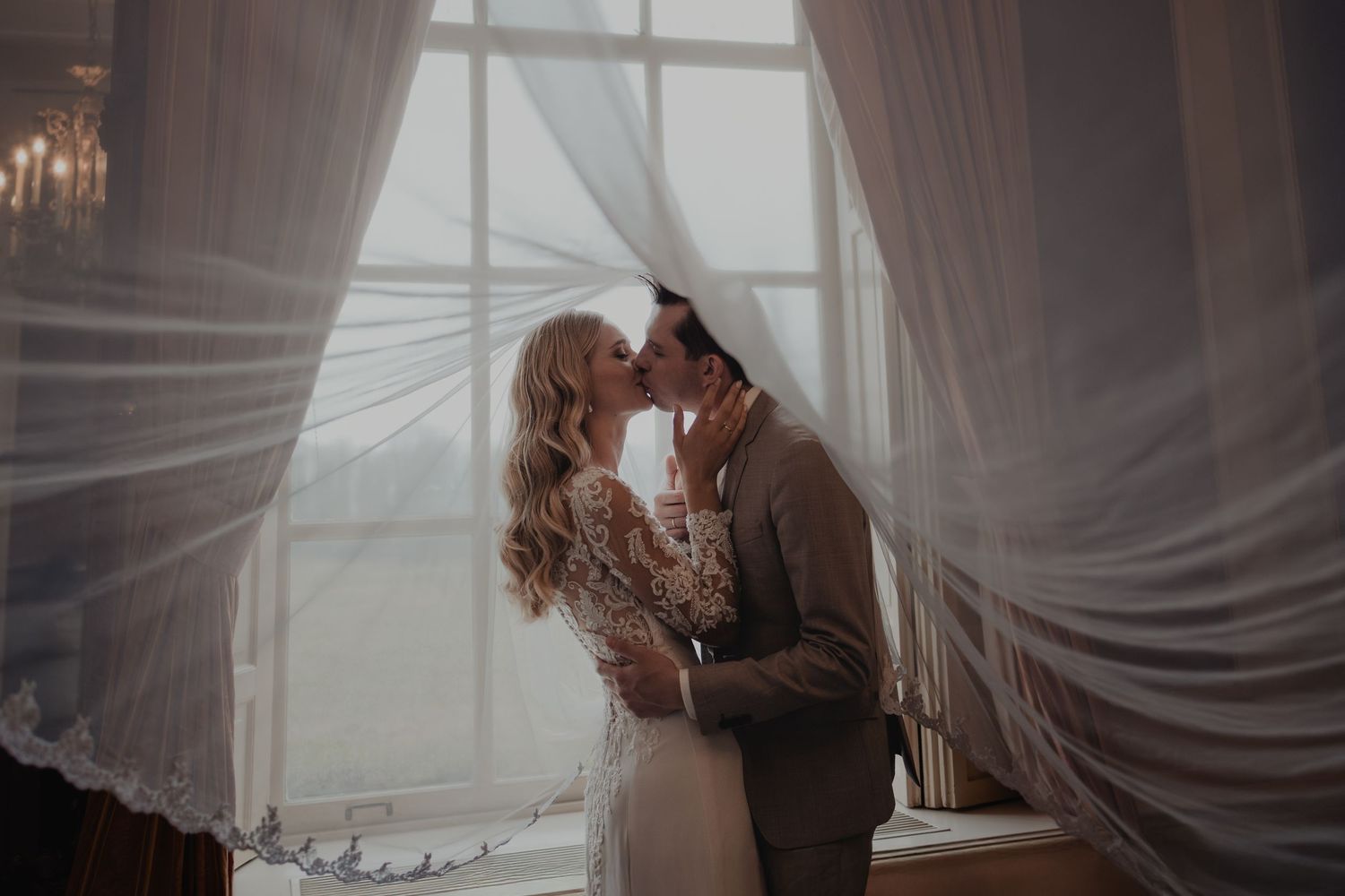 Romantic couple embraces in a dreamy setting with flowing white curtains and soft lighting.