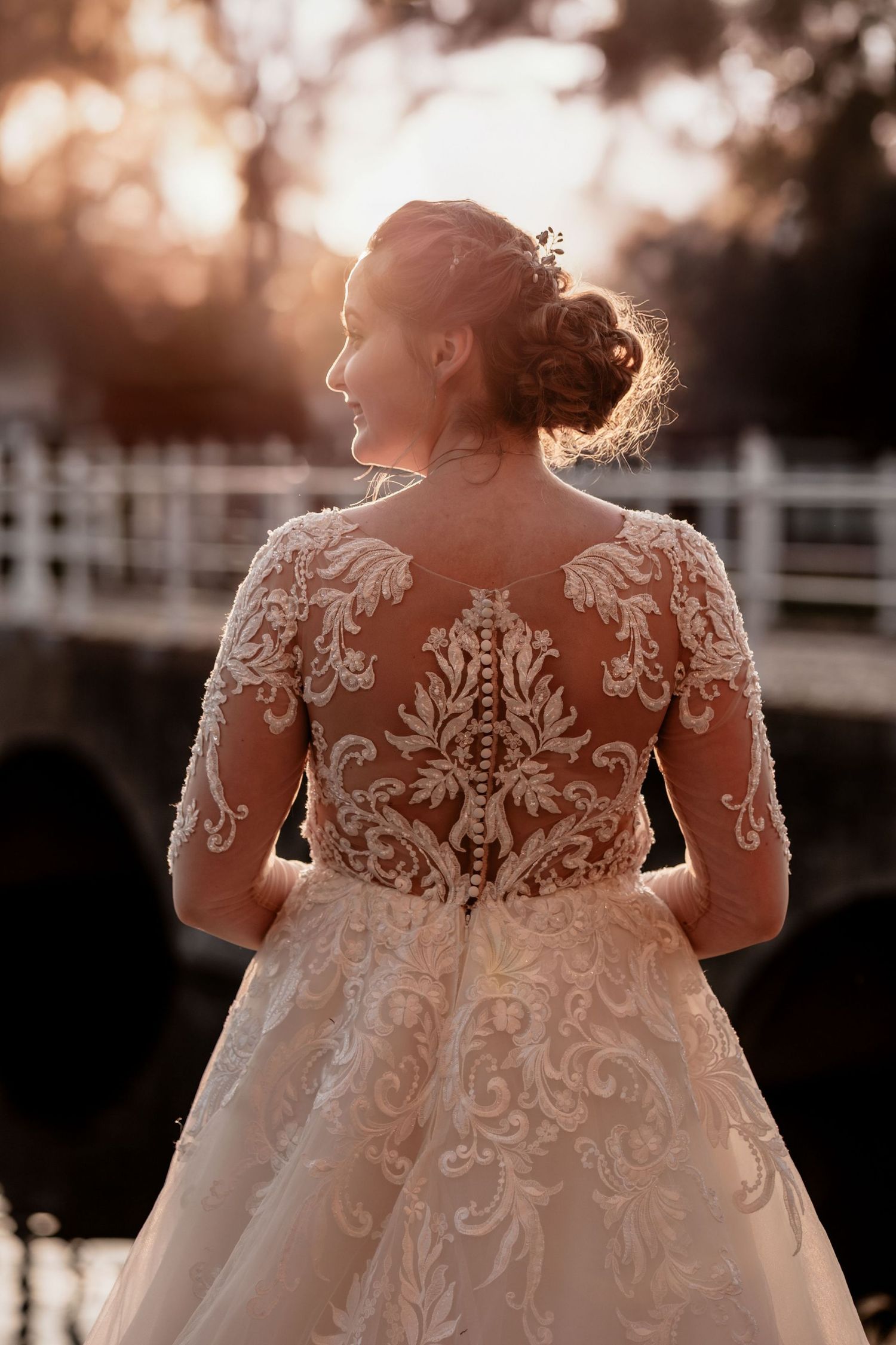 Back view of a wedding dress with intricate lace detailing and floral appliques glowing in sunset light.