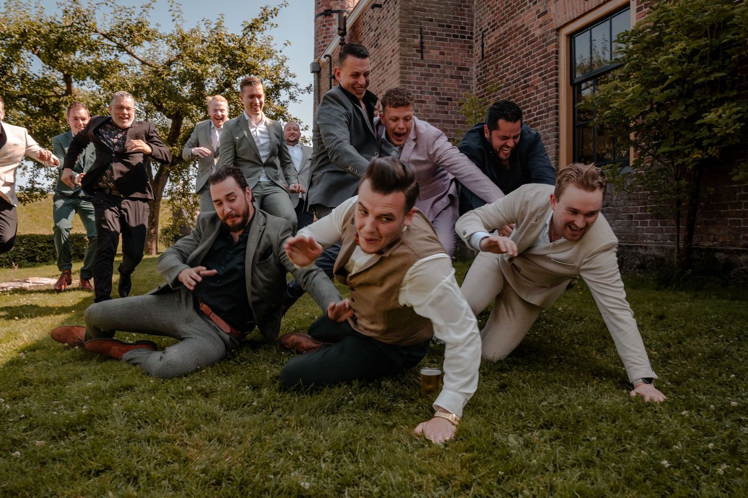 Group lying on grass in playful pose during outdoor wedding photo session.