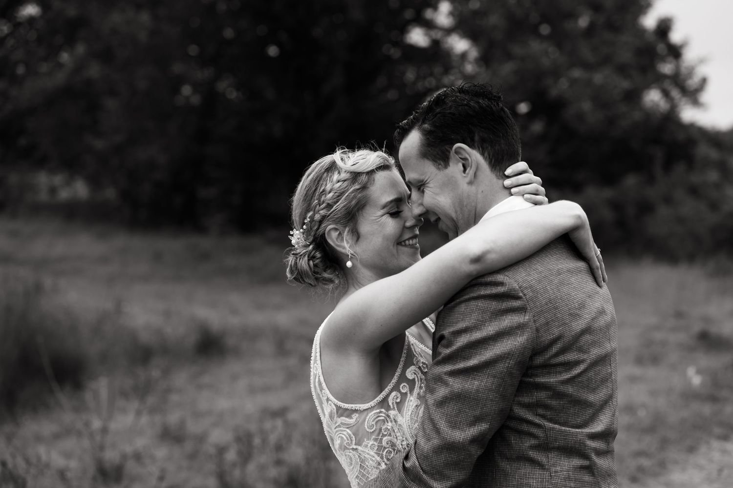 A tender romantic embrace between two people dancing outdoors in formal wedding attire.