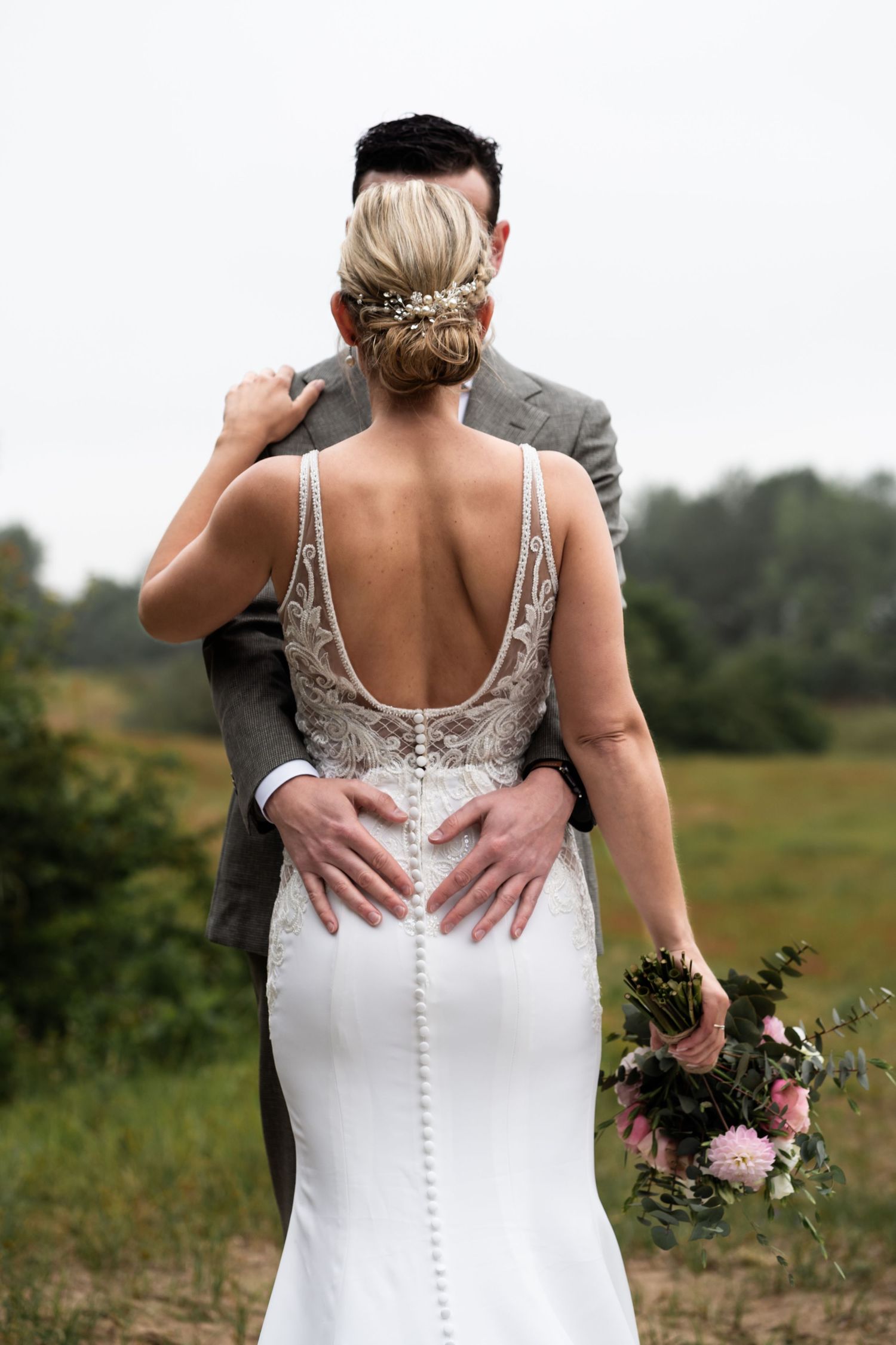Back view of a bride in a fitted lace dress with intricate button details and elegant updo hairstyle.