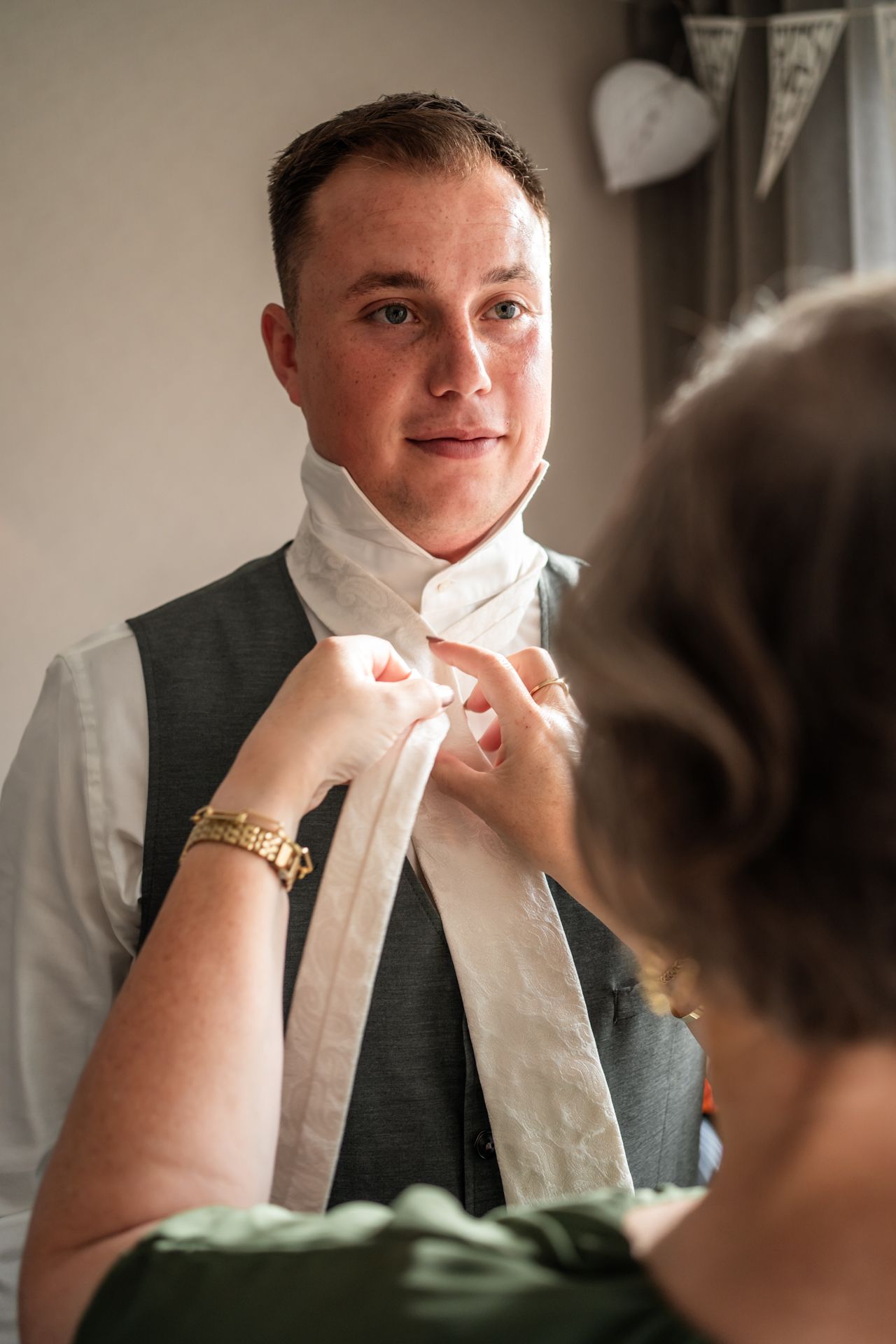 A helping hand adjusts a white tie during wedding preparation.