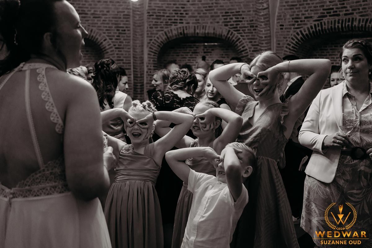 Candid wedding reception moment showing guests dancing and socializing in front of a brick wall backdrop.