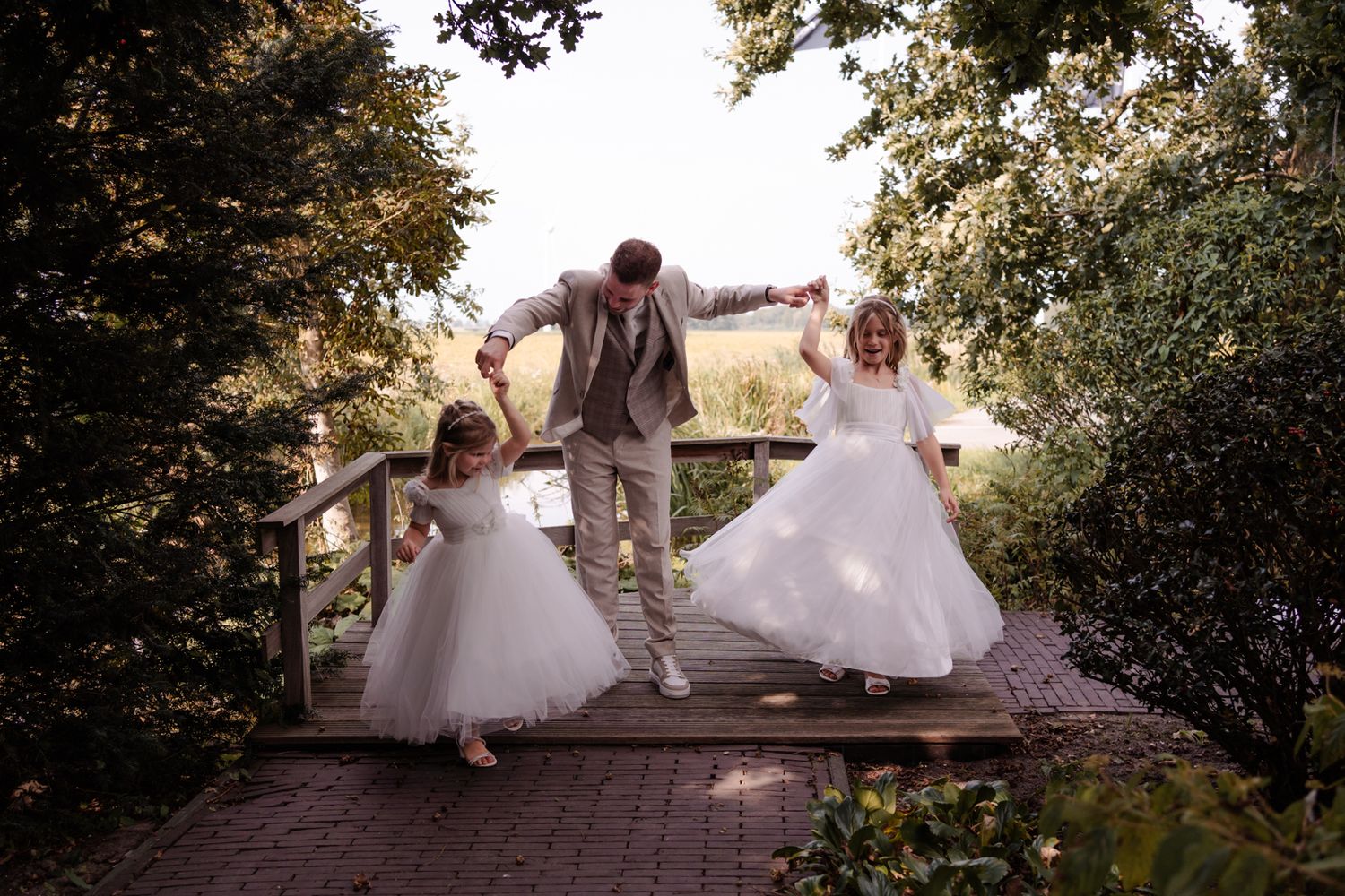 Playful wedding photo of couple jumping on wooden bridge in garden setting.