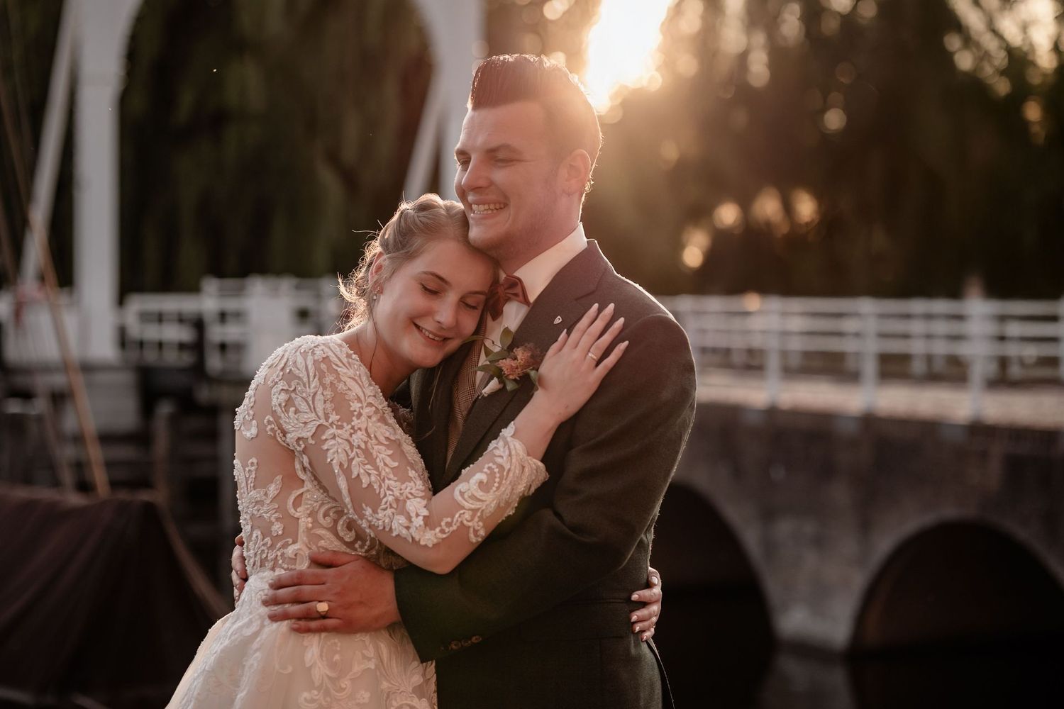 A couple shares a romantic moment at sunset on a dock, surrounded by golden light and reflections on the water.