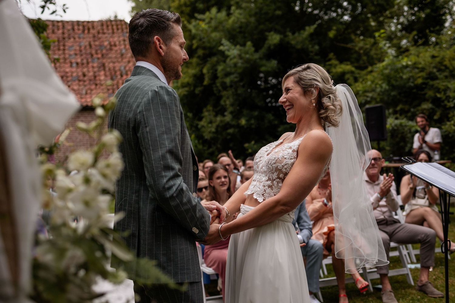A joyful outdoor wedding ceremony with a couple holding hands at the altar while guests look on in a garden setting.