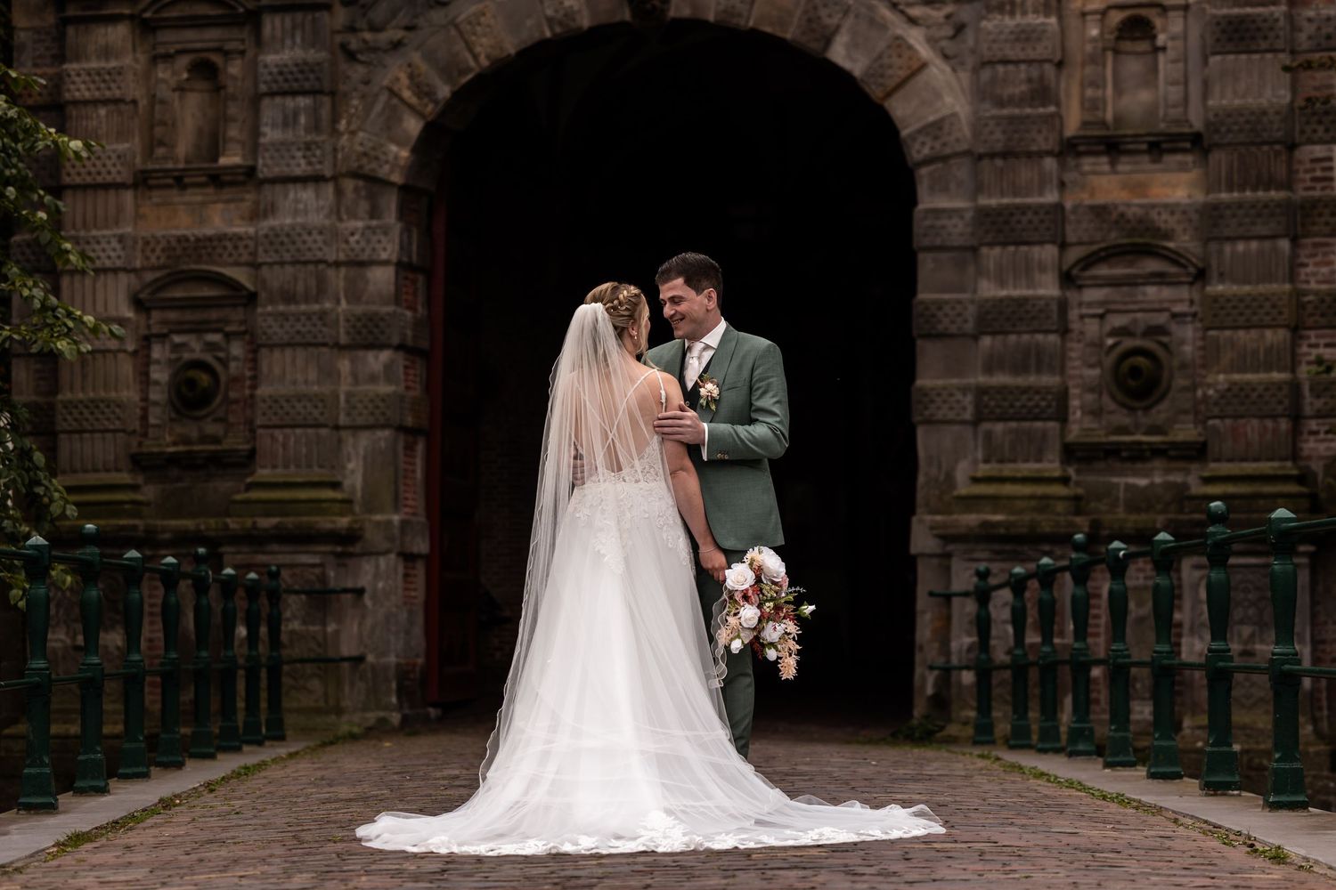 A wedding couple stands in front of a historic stone church archway during their romantic outdoor ceremony.