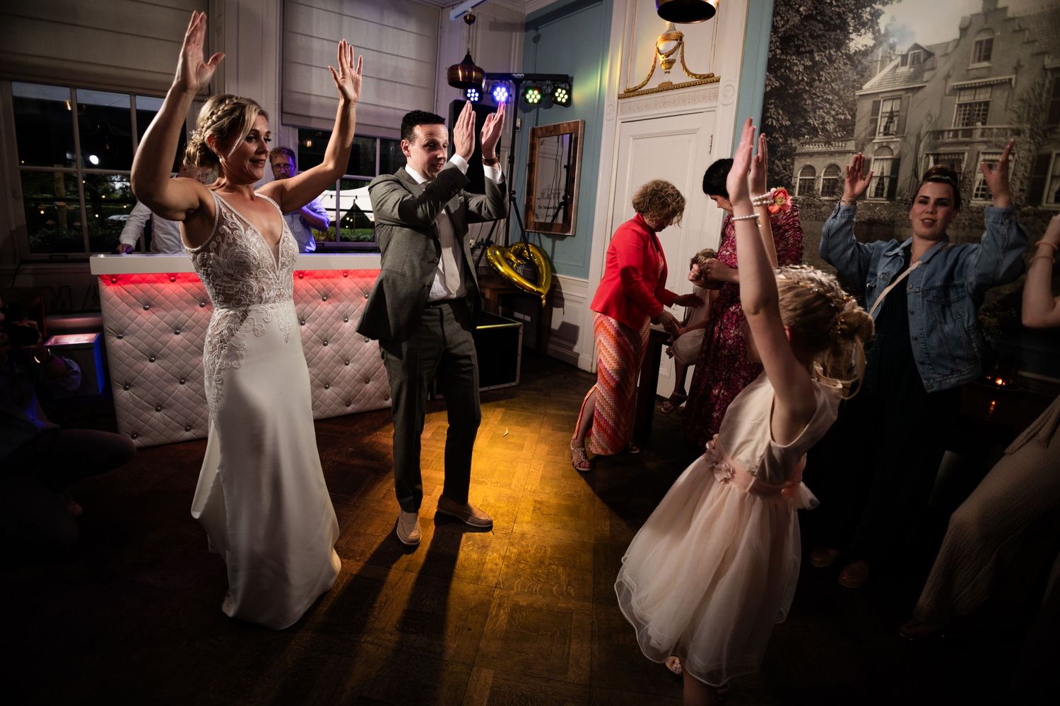 Wedding celebration on dance floor with people dancing under colorful lights.