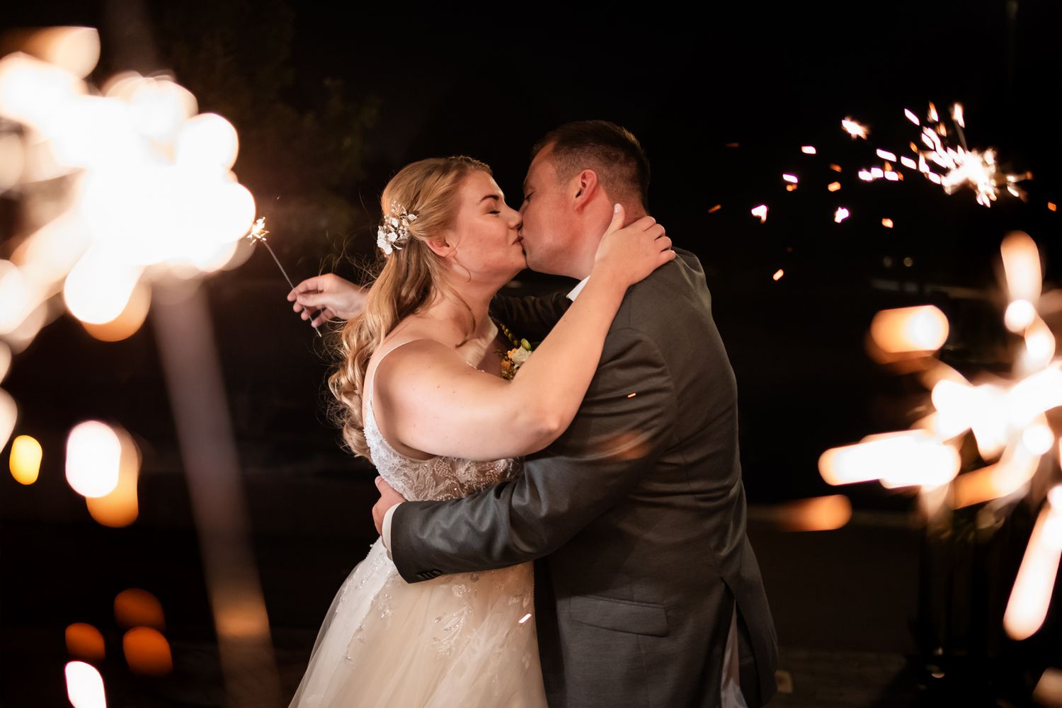 Romantic nighttime wedding kiss surrounded by sparkling sparklers.
