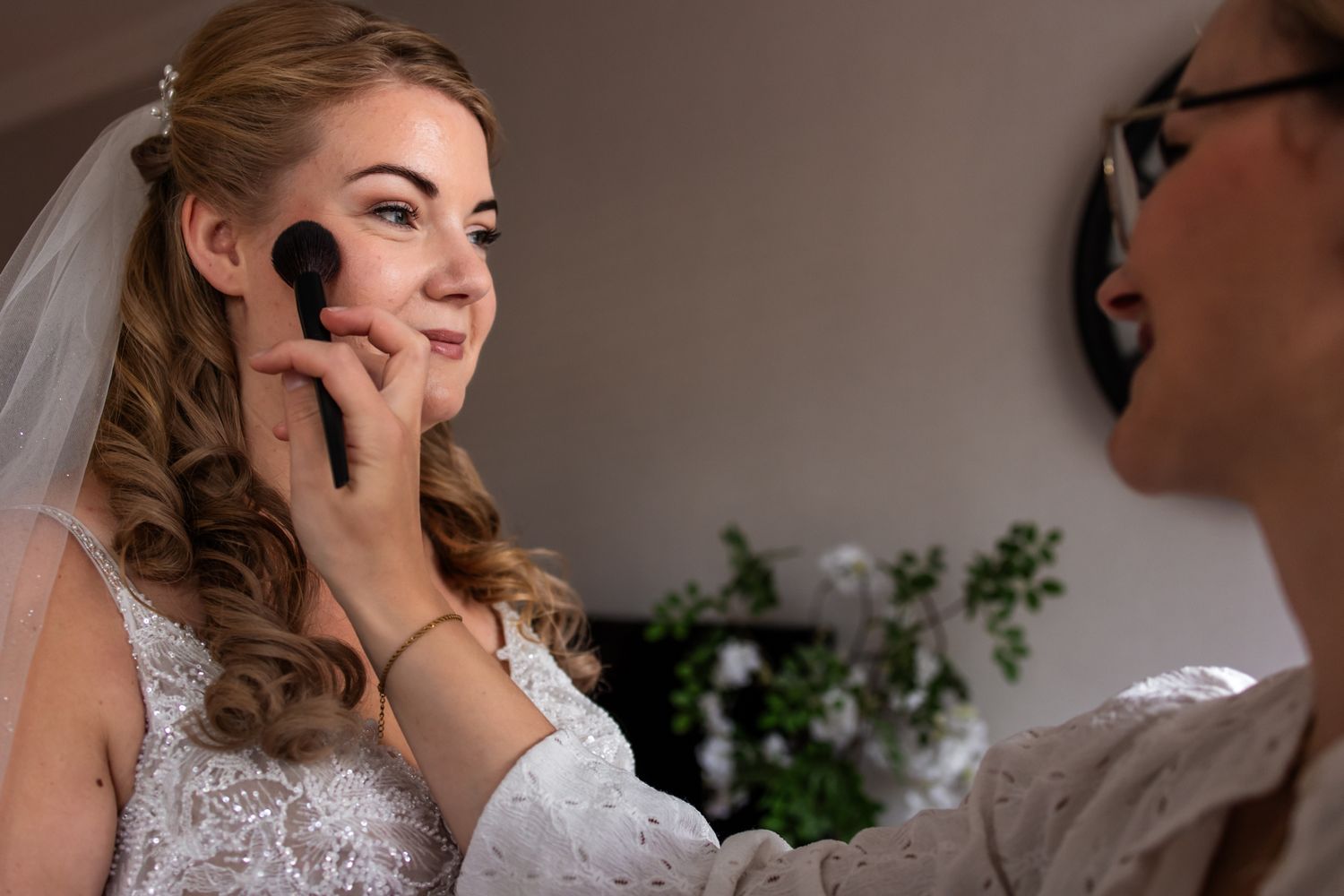 Makeup artist applies finishing touches to bride's face with brush during wedding preparation.