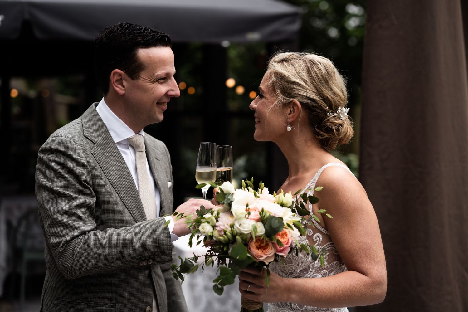 A celebratory toast between newlyweds with champagne glasses and white floral bouquet.