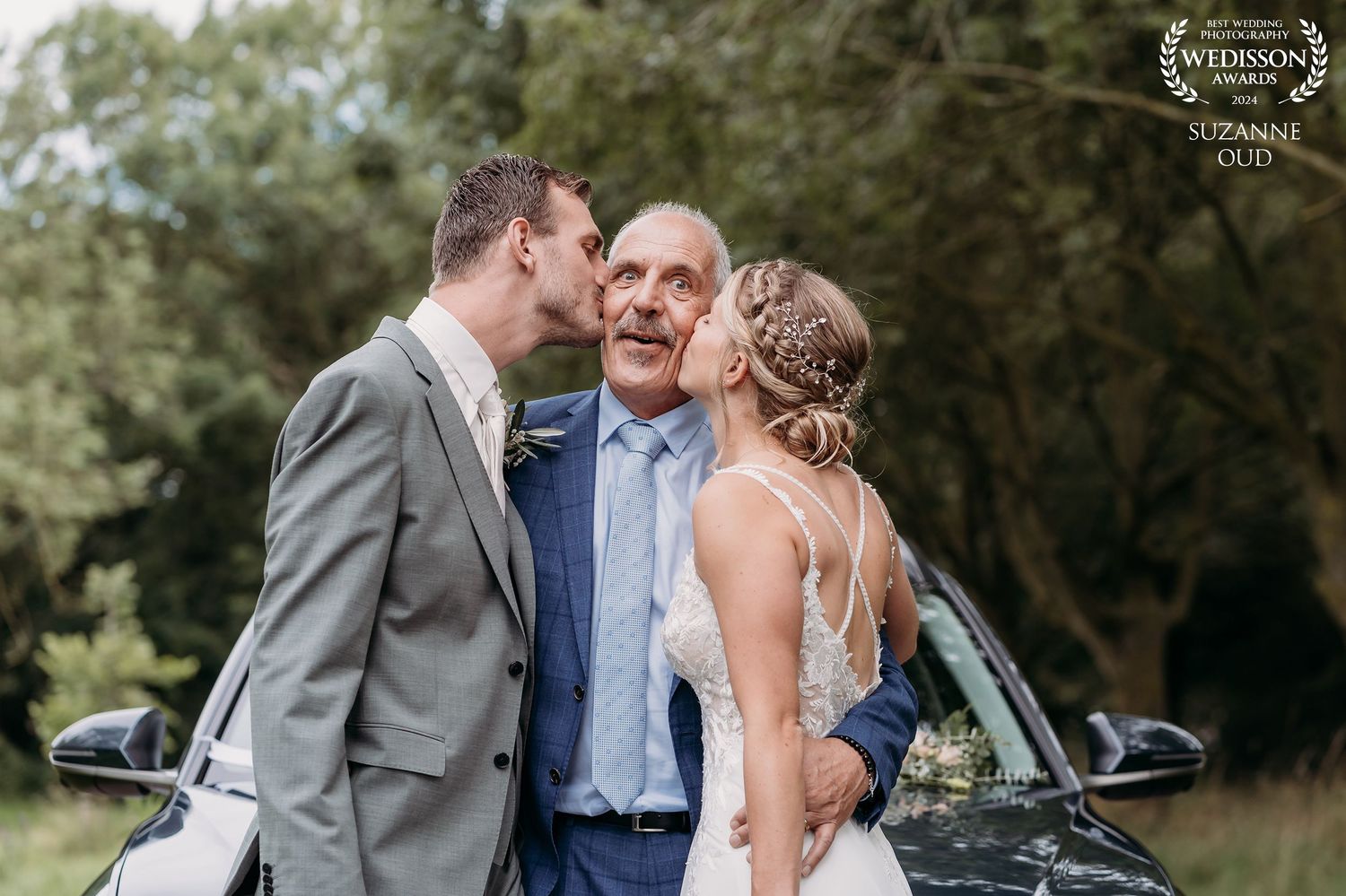 Wedding day portrait near vintage car with gentle moment between wedding party members.