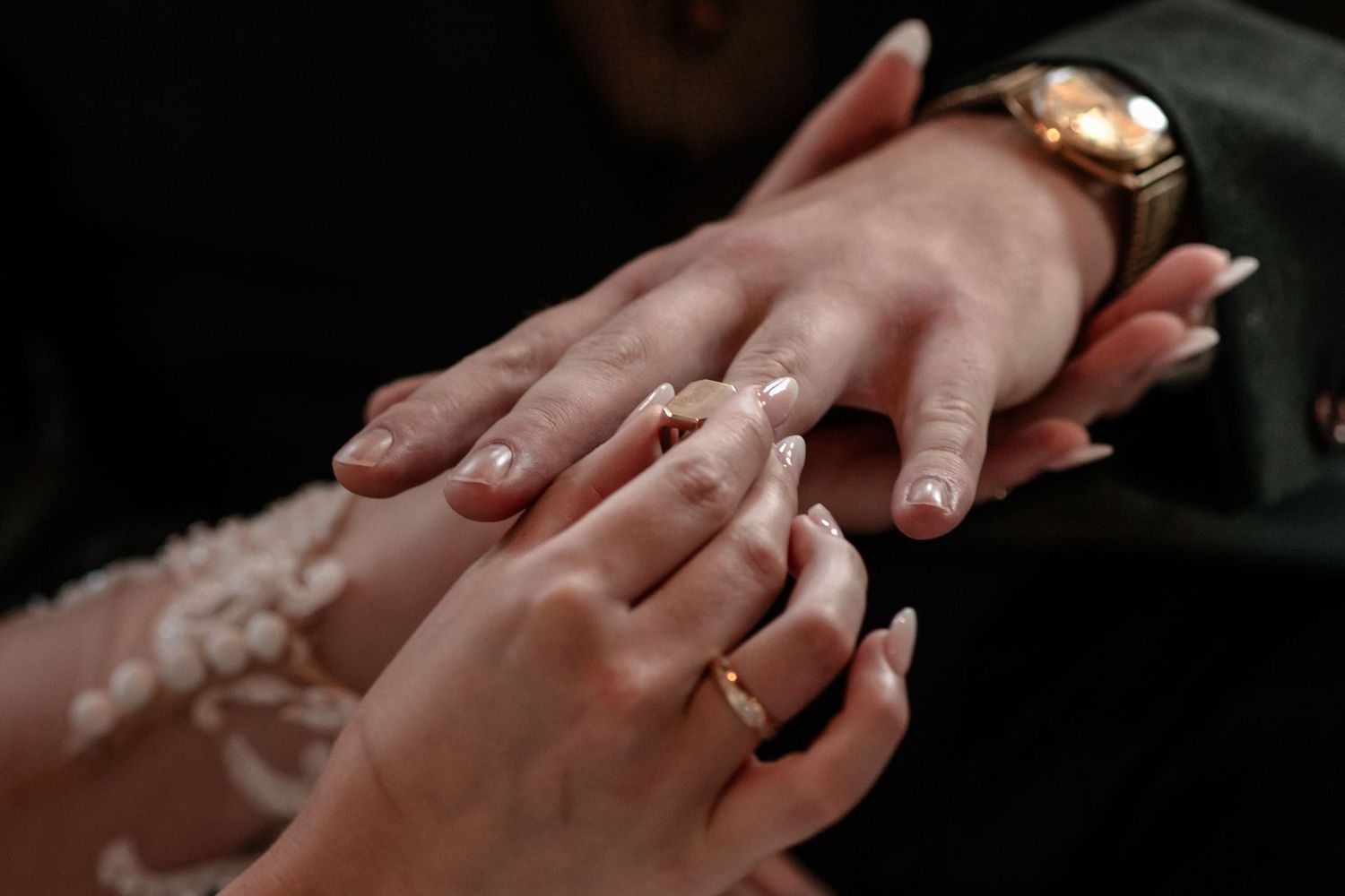 A close-up shot of hands exchanging wedding rings during a ceremony, with elegant jewelry visible.