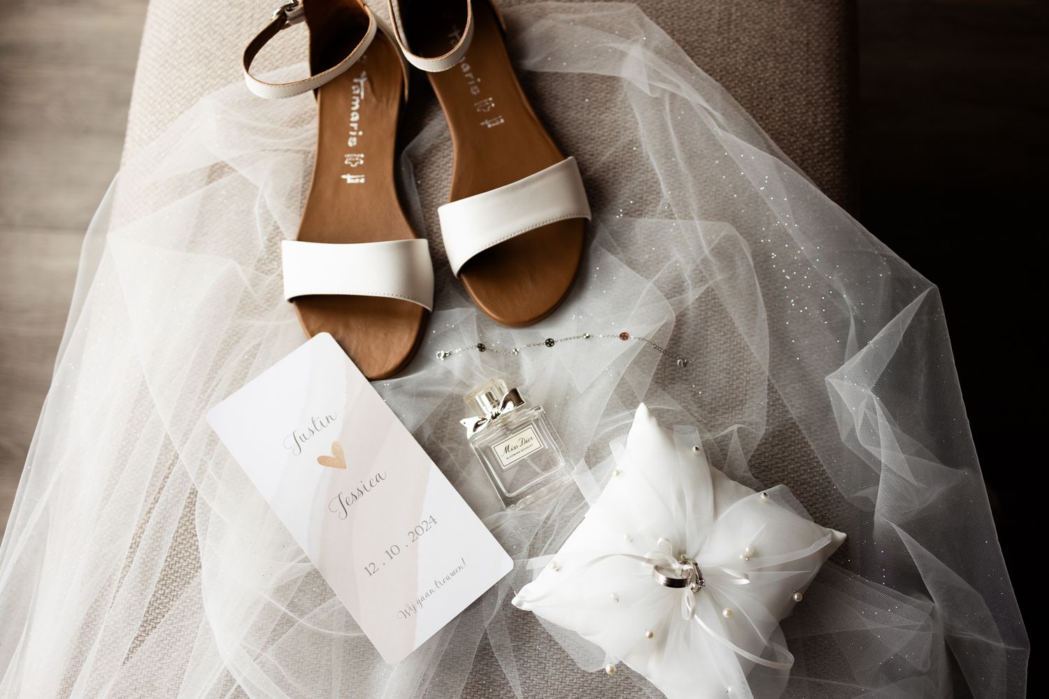 Wedding detail shot of white sandals, veil, and delicate floral accessories on rustic surface.