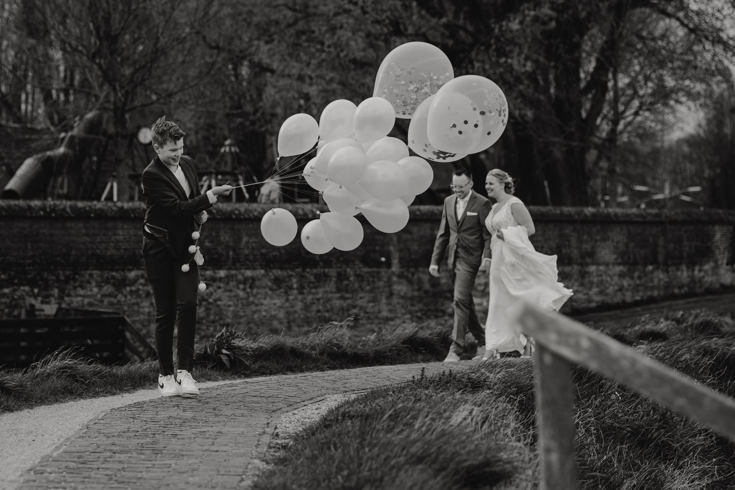 Black and white wedding photo with white balloons in garden setting.