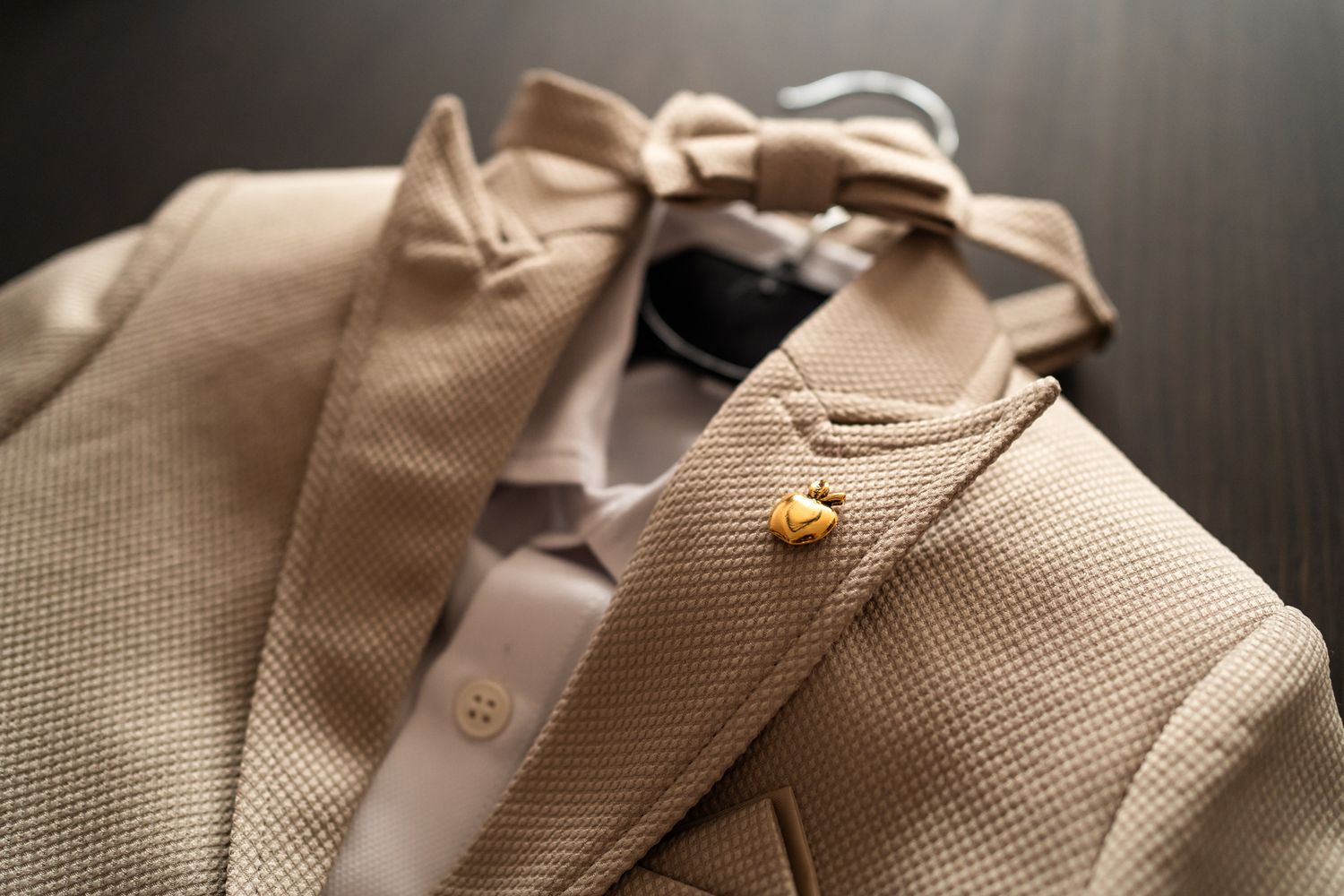 Close-up view of a beige textured suit jacket with a small golden lapel pin detail.
