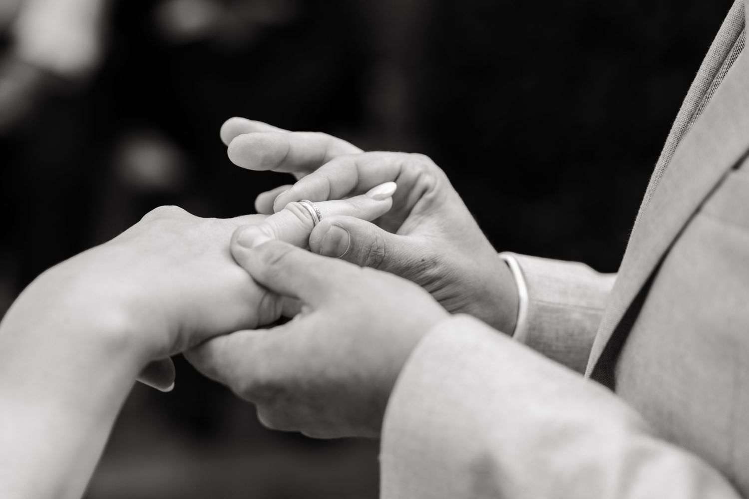 Black and white close-up photo of hands exchanging wedding rings during a marriage ceremony.