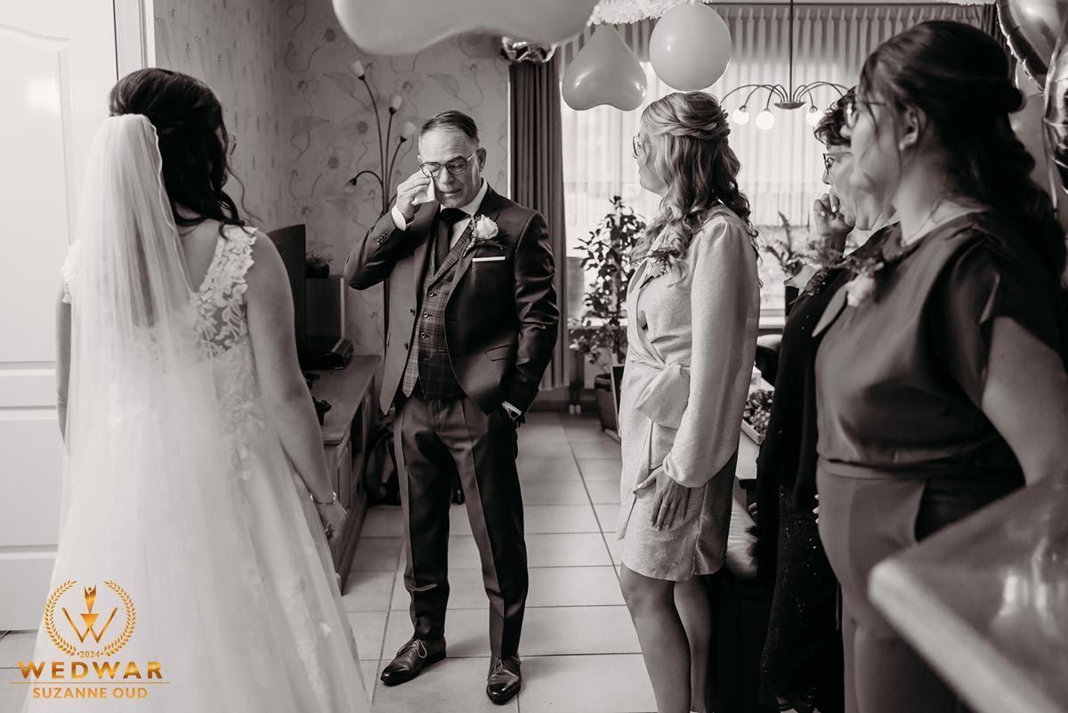 Black and white candid moment from wedding preparations with white gown visible.
