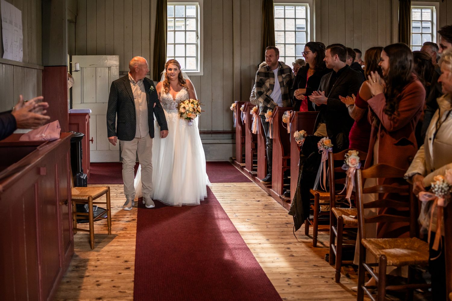 Wedding ceremony in historic church with wooden pews and red carpet aisle.