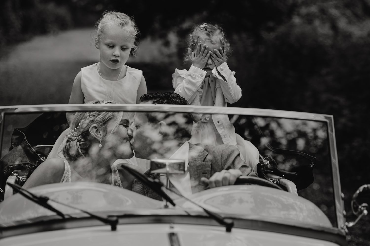 A vintage black and white photo shows children sitting in the back of a convertible car.