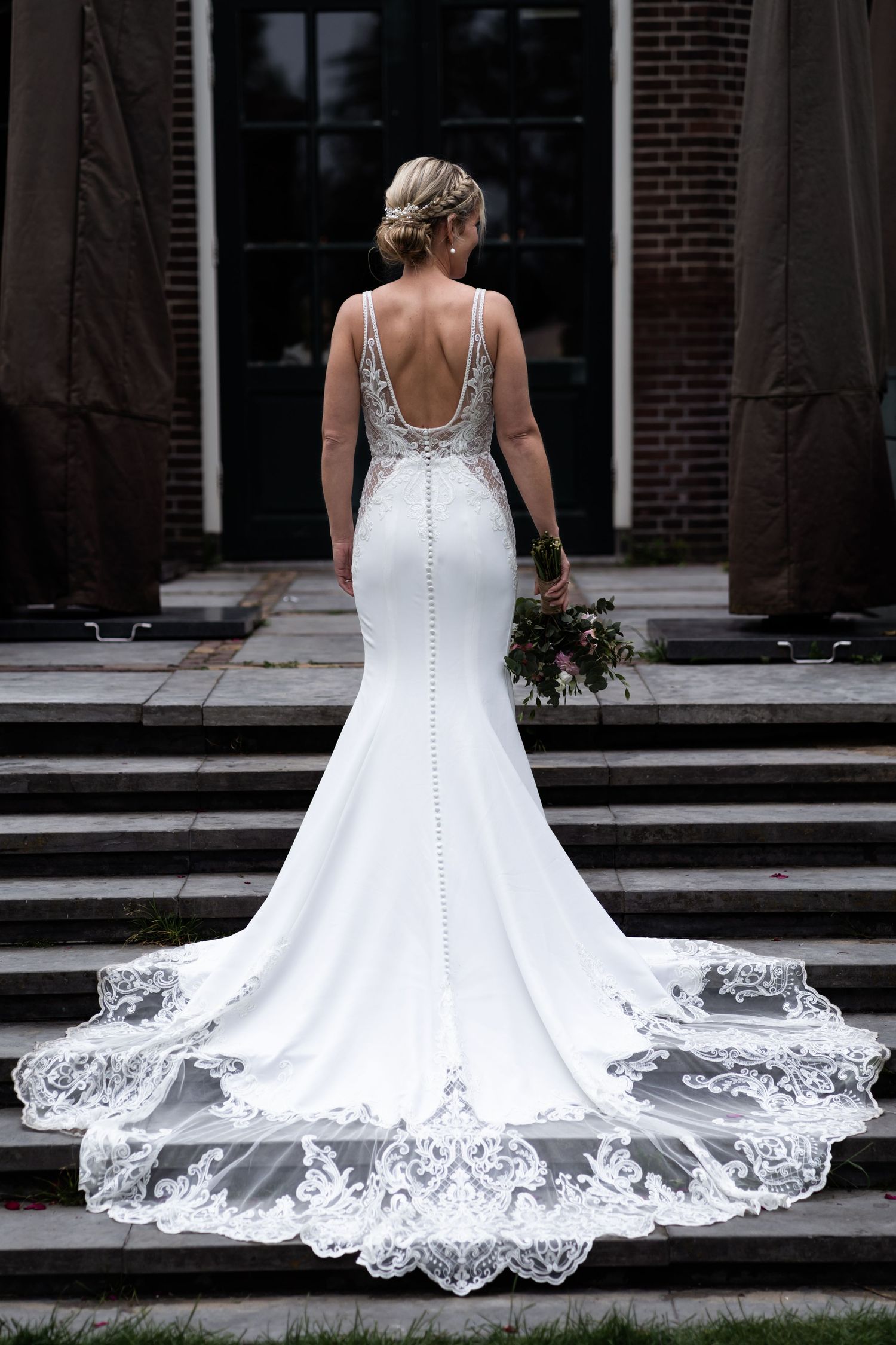 Elegant mermaid wedding gown with detailed lace train on stone steps.