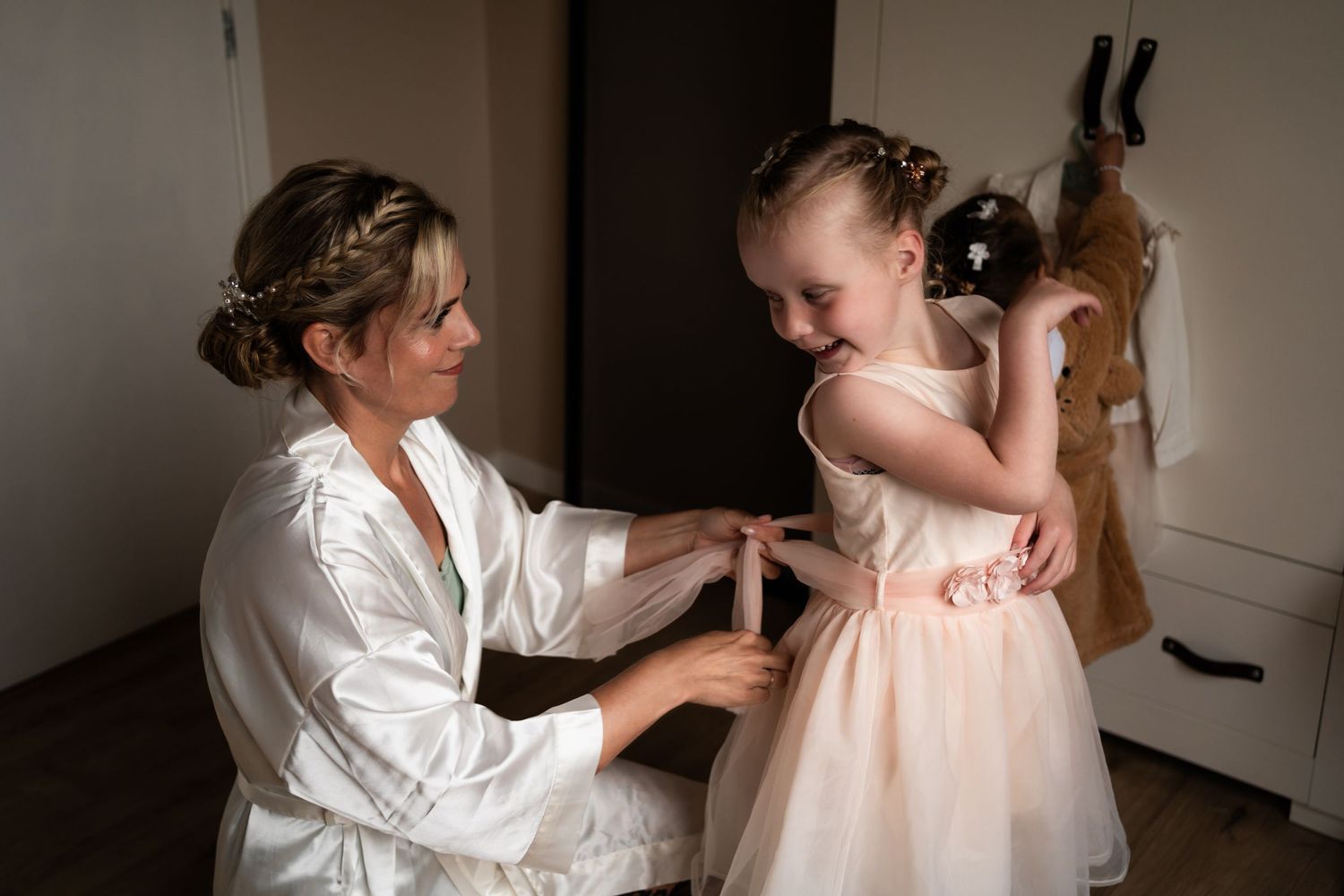 A touching moment showing final wedding preparations with a flowing pink dress and a cat photobombing in the background.