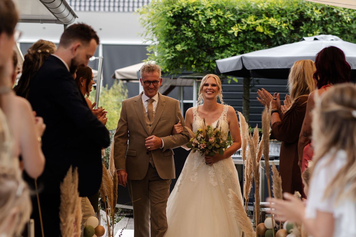 Wedding ceremony processional under a white tent with greenery in the background.