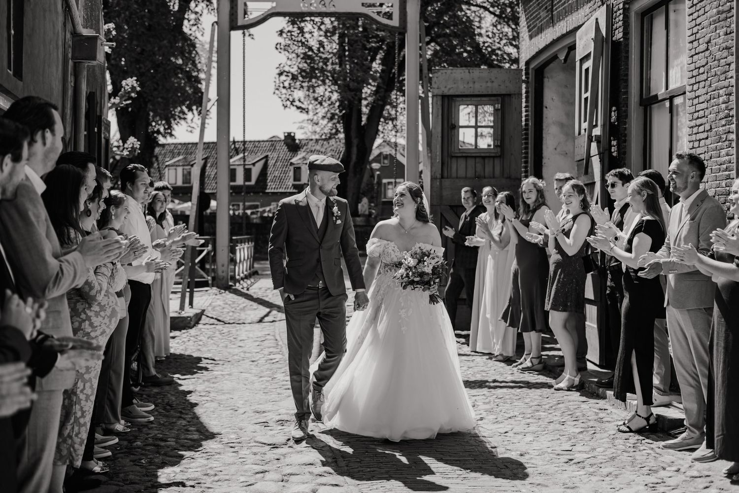 Black and white wedding photo of bride and groom walking through cheering guests outdoors.