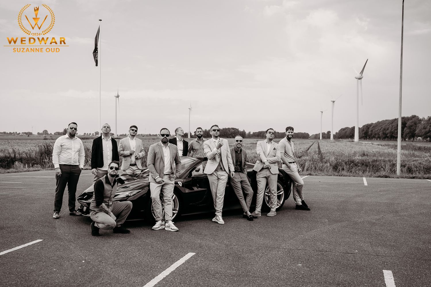 Groomsmen posing casually with vintage car in black and white outdoor photo.