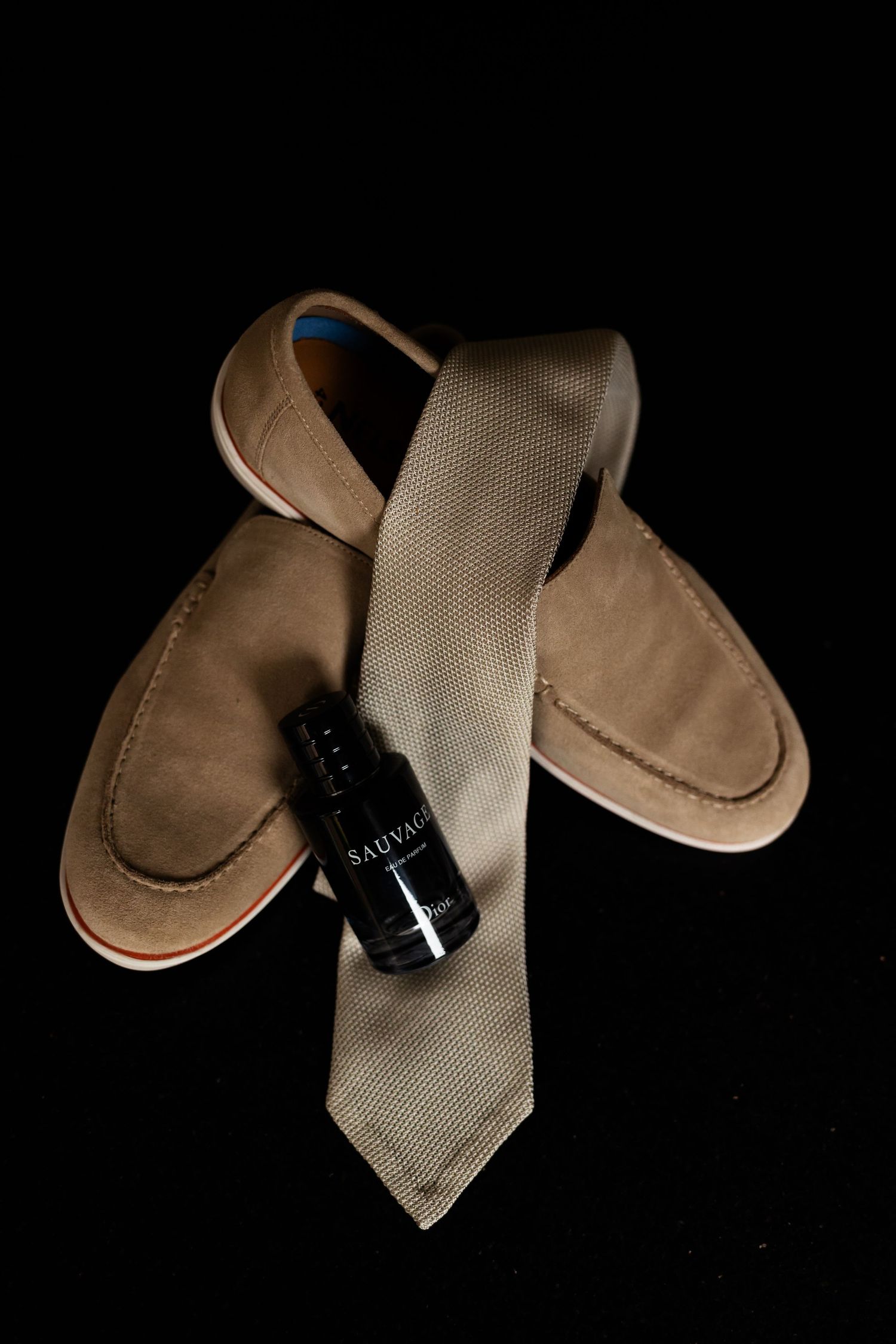 Classic brown leather loafers with a beige tie and small perfume bottle on black background.