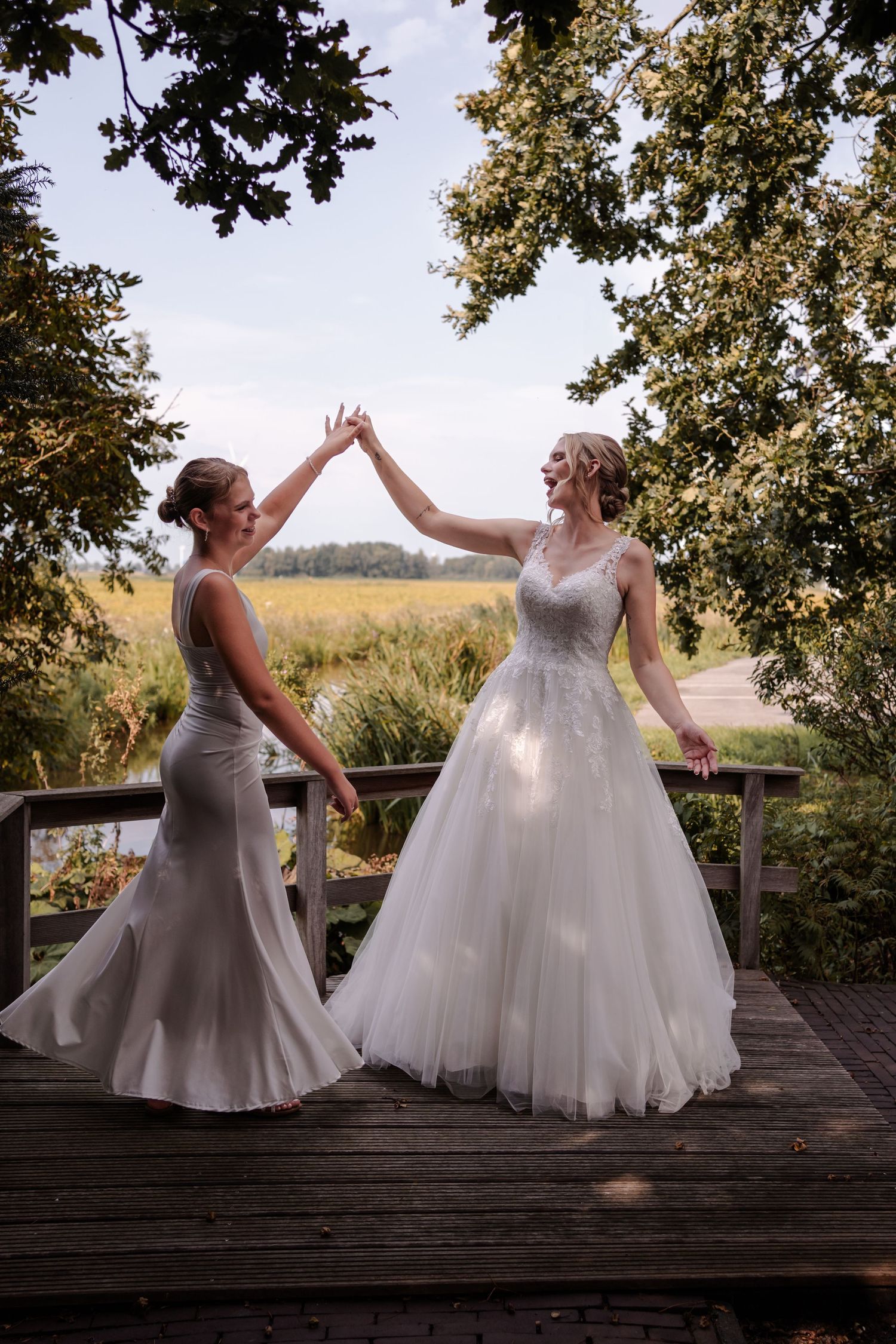 Two people in formal dresses share a high-five moment on a wooden deck surrounded by trees and natural scenery.
