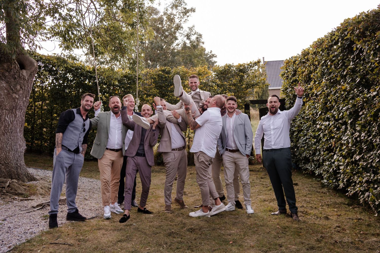 Celebratory group photo with wedding party in coordinated attire jumping and cheering outdoors.