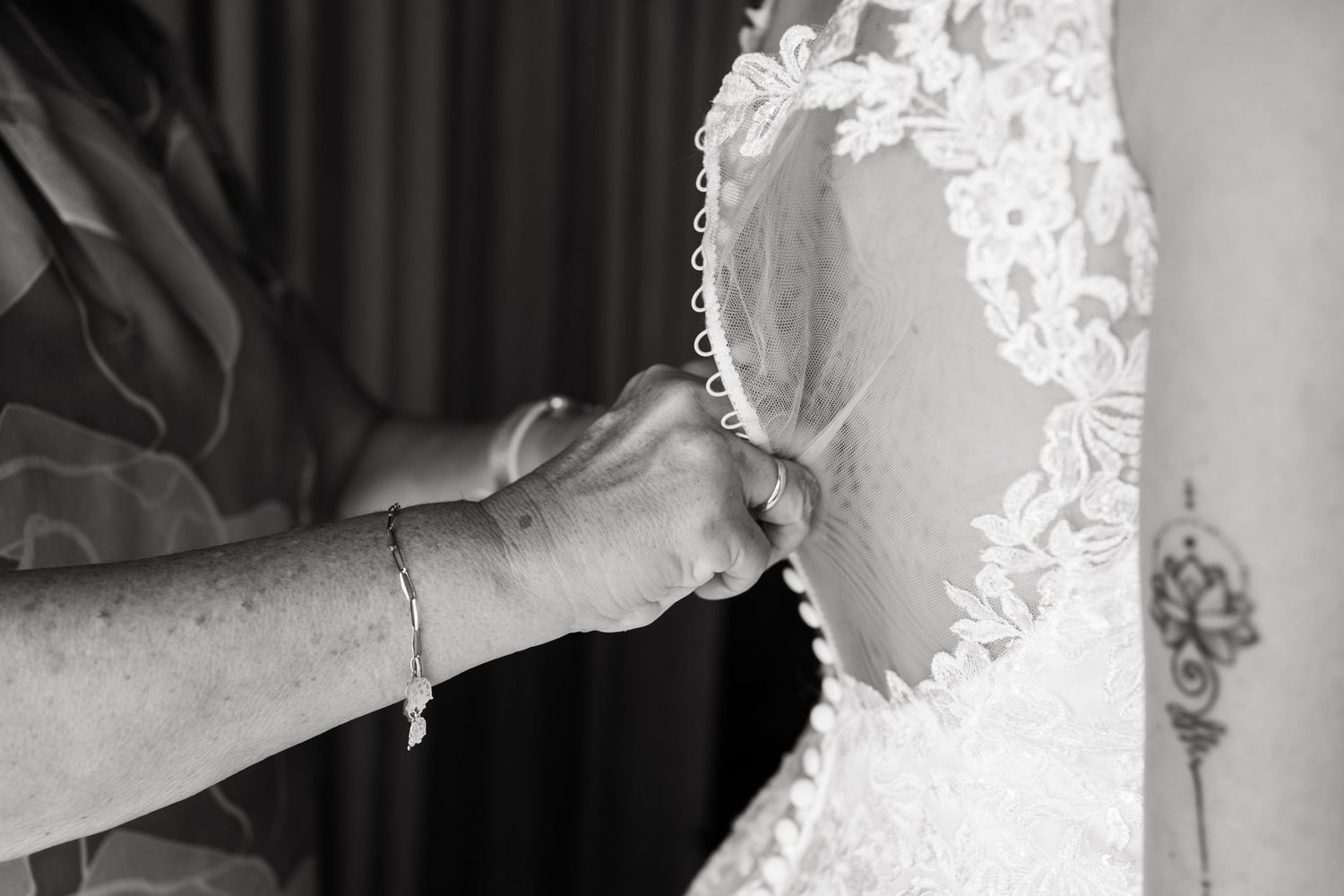 Black and white closeup photo of hands adjusting delicate lace details on a wedding dress sleeve.