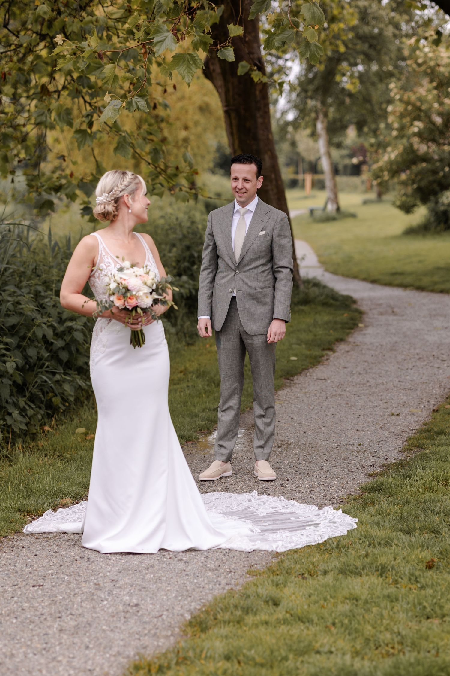 A wedding couple poses on a garden path, with the bride wearing a flowing white dress and holding a bouquet.
