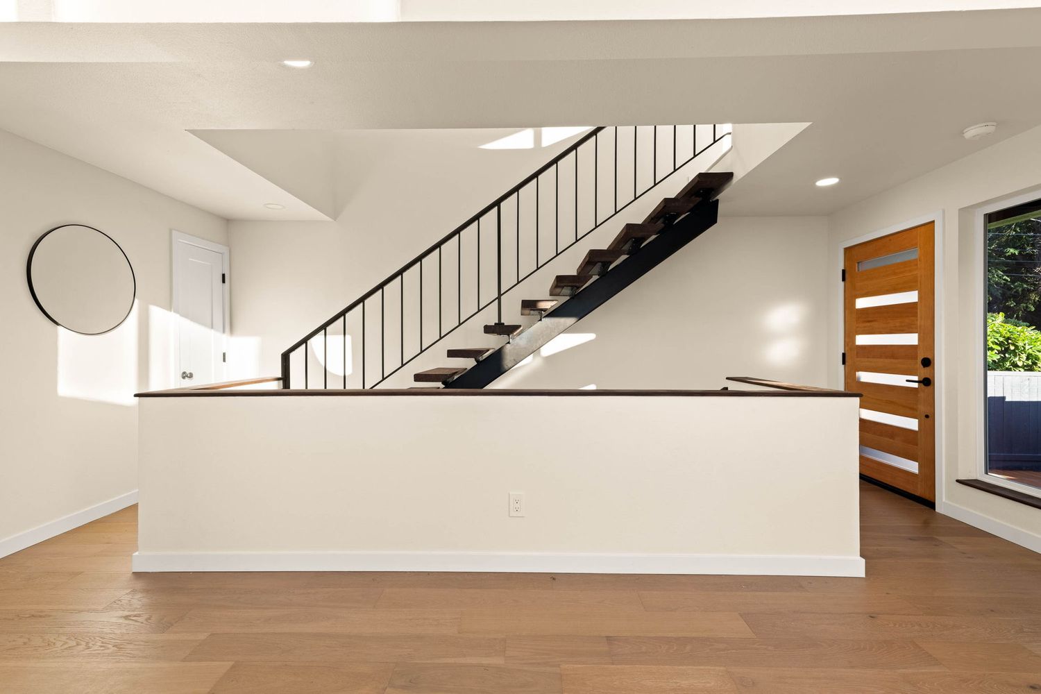 Contemporary open concept living space with white walls, hardwood flooring, and a staircase features natural lighting.