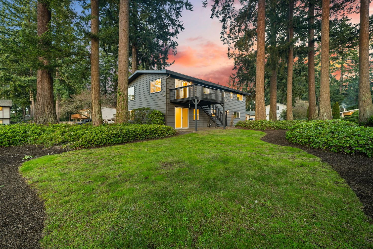Wooded hillside with evergreen trees and residential buildings at sunset creating a peaceful suburban landscape.